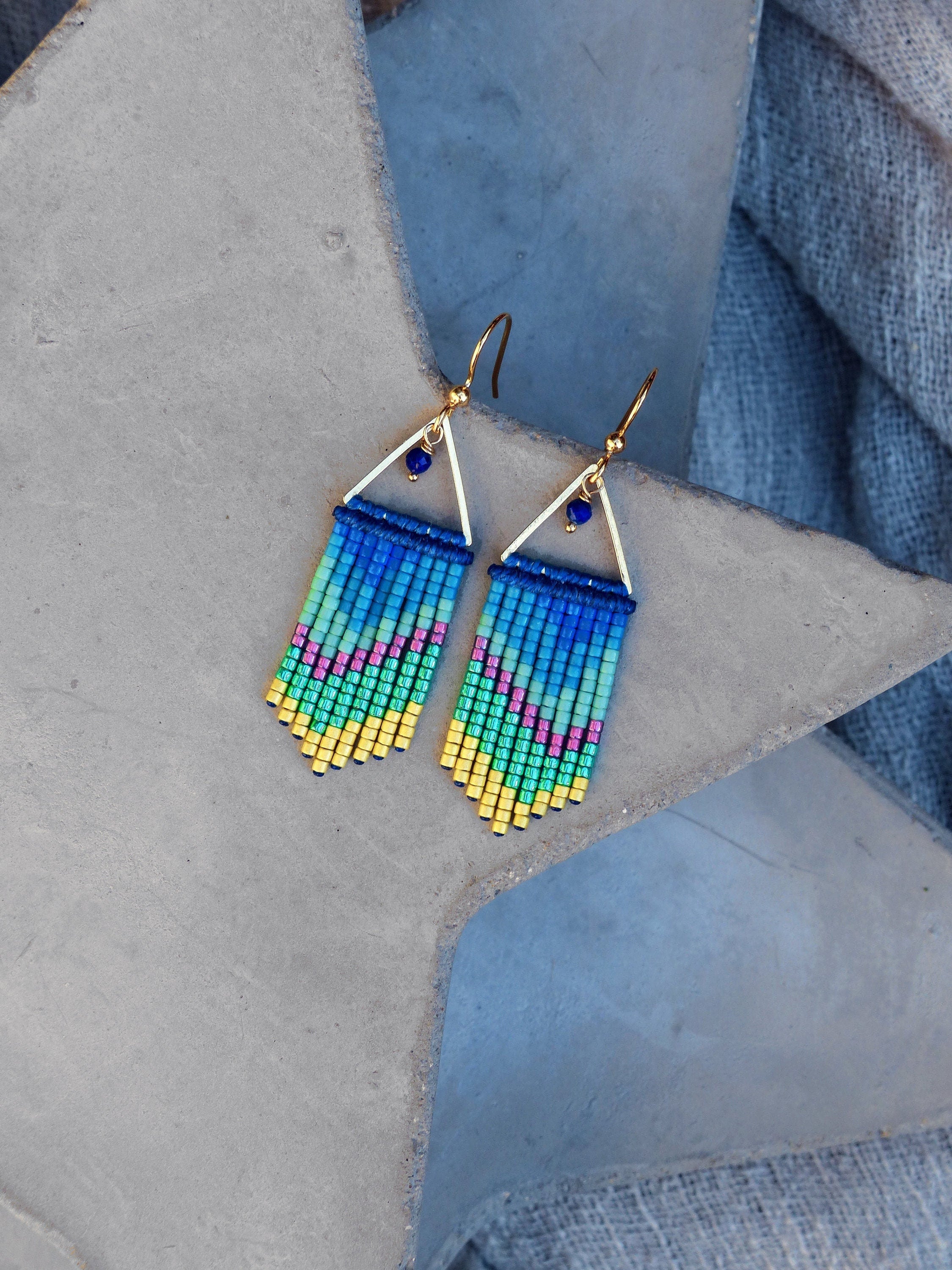 Peut inclure: Une paire de boucles d'oreilles pendantes en forme de triangle doré avec des franges de perles bleues, vertes, jaunes et roses.
