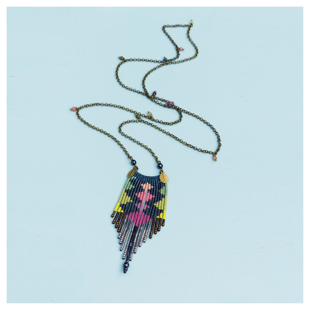 Peut inclure: Un long collier de perles avec un pendentif géométrique coloré. Le pendentif est fait de petites perles colorées et a une frange de perles argentées et dorées.