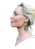 Peut inclure: Une femme aux cheveux blonds portant une chemise blanche et un collier en or avec un pendentif en cristal. Elle porte de longues boucles d'oreilles en perles turquoise, blanches et dorées.