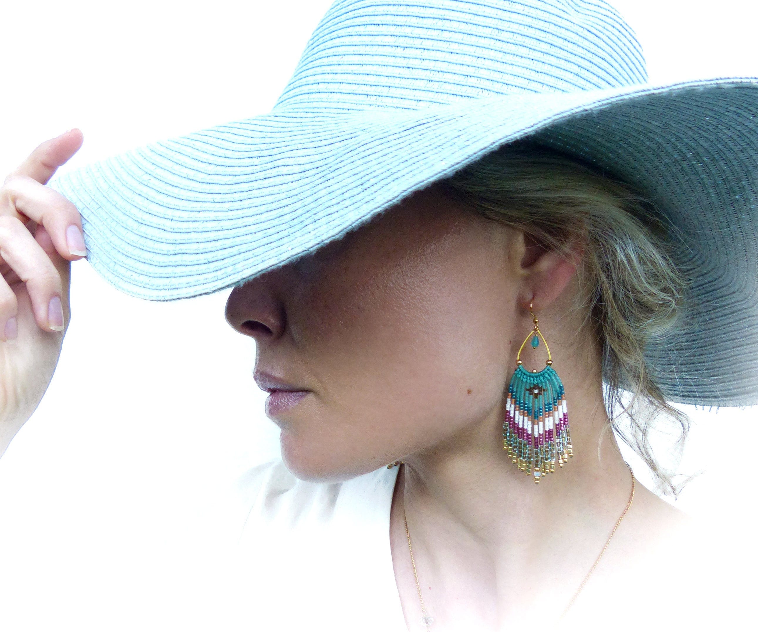 Peut inclure: Une femme portant un chapeau de soleil bleu clair à large bord et de longues boucles d'oreilles en perles avec des accents turquoise, blanc, rose et or.