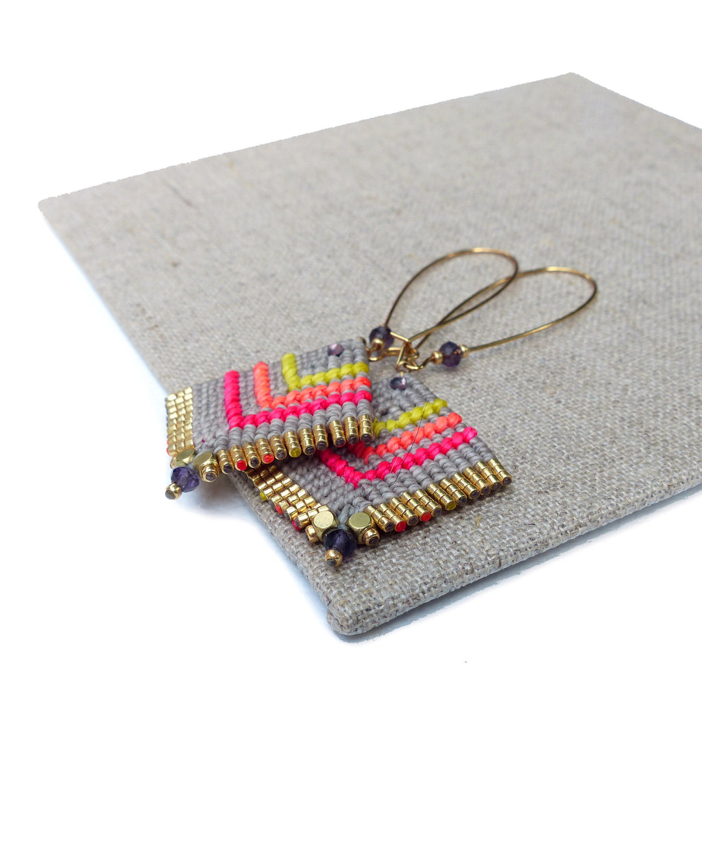 Peut inclure: Une paire de boucles d'oreilles géométriques avec un motif gris, rose et jaune. Les boucles d'oreilles sont faites de petites perles et ont des accents dorés.