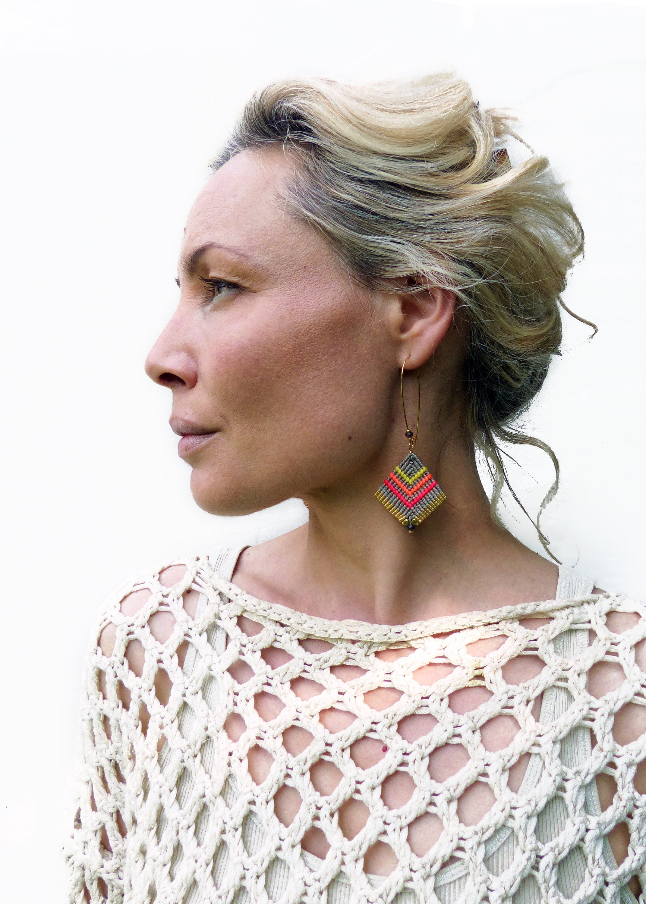 Peut inclure: Une femme portant un haut en crochet blanc avec une paire de boucles d'oreilles géométriques en forme de diamant. Les boucles d'oreilles sont faites de fil coloré et ont un anneau en or.