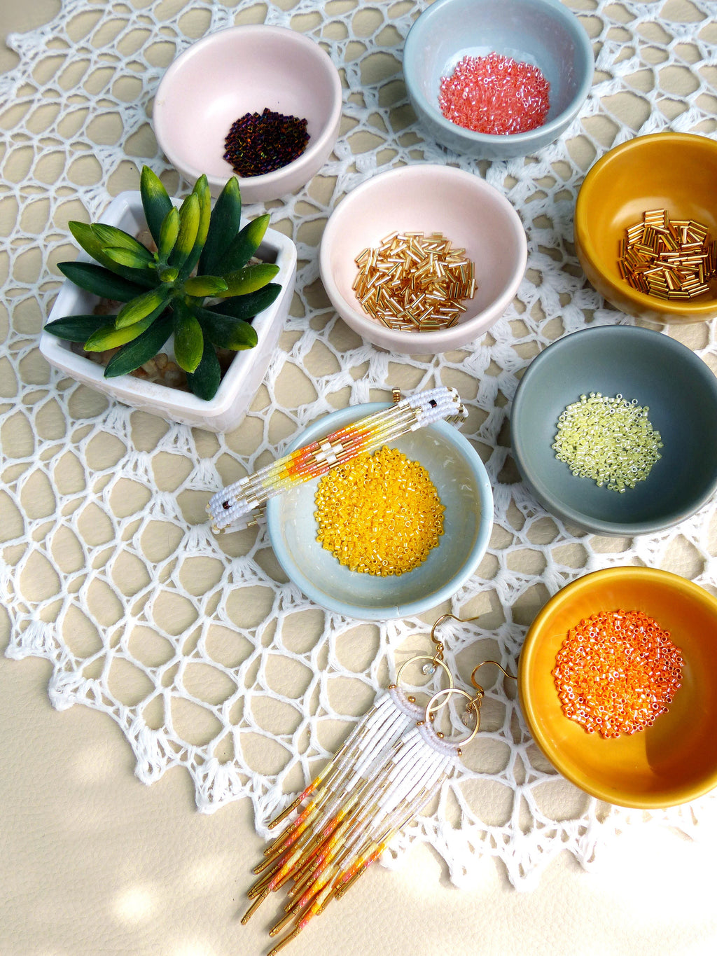 Peut inclure: Un assortiment de perles colorées dans de petits bols, y compris de l'or, de l'orange, du rose, du jaune et du vert. Un bracelet en perles blanches et des boucles d'oreilles assorties sont également présentés.