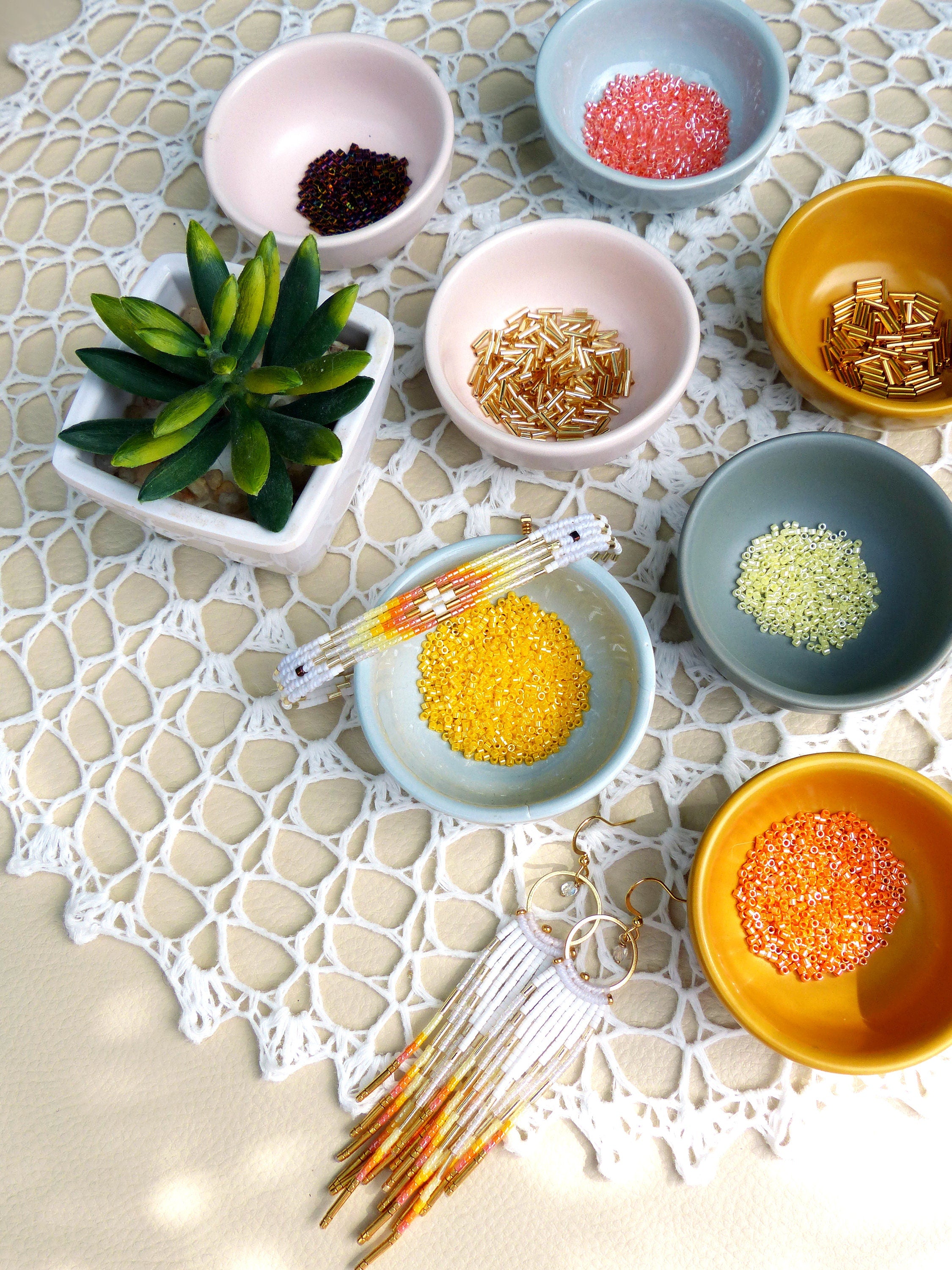 Peut inclure: Un assortiment de perles colorées dans de petits bols, y compris de l'or, de l'orange, du rose, du jaune et du vert. Un bracelet en perles blanches et des boucles d'oreilles assorties sont également présentés.