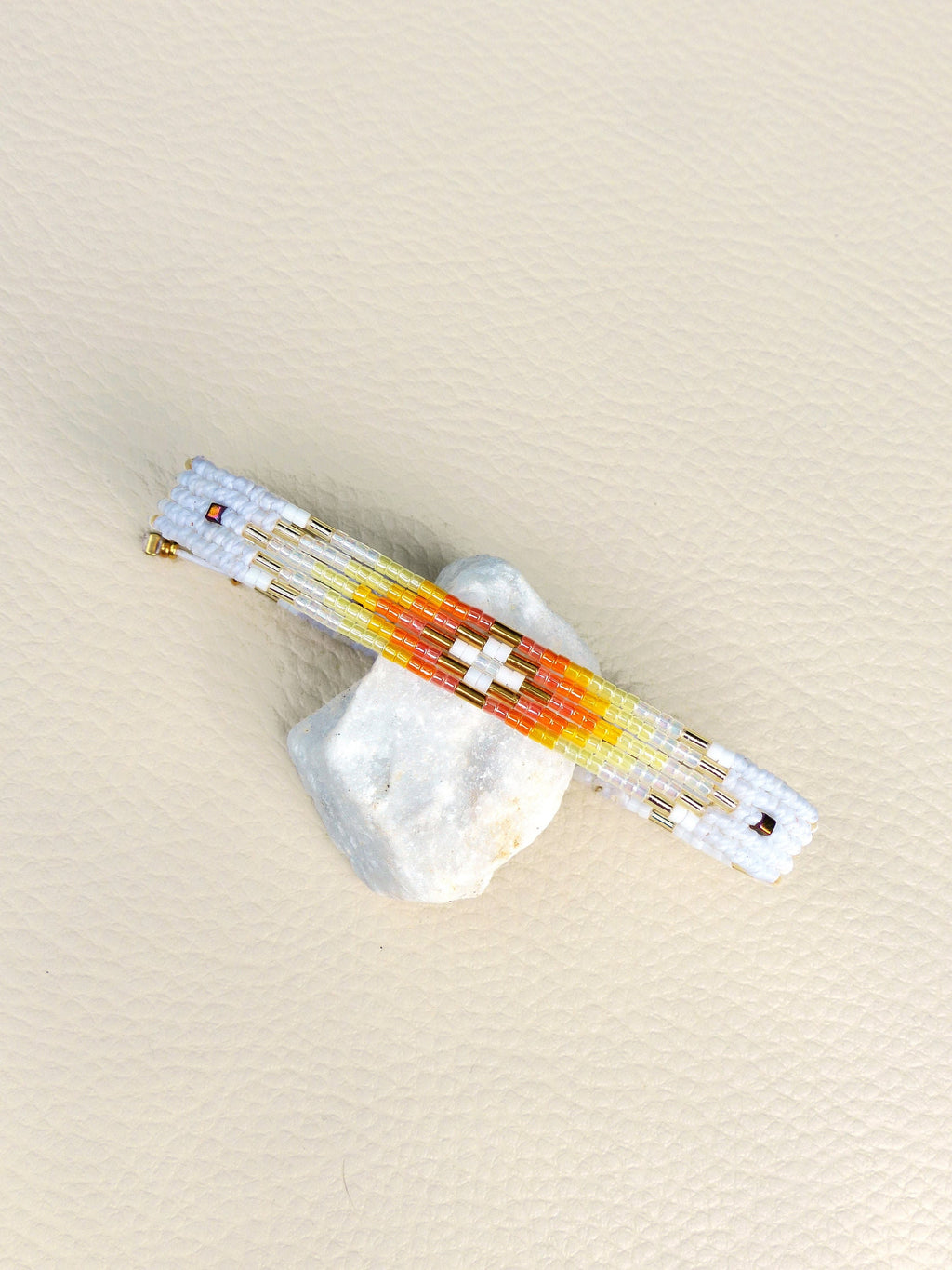 Peut inclure: Une pince à cheveux en perles blanches, jaunes, orange et dorées avec un motif géométrique.