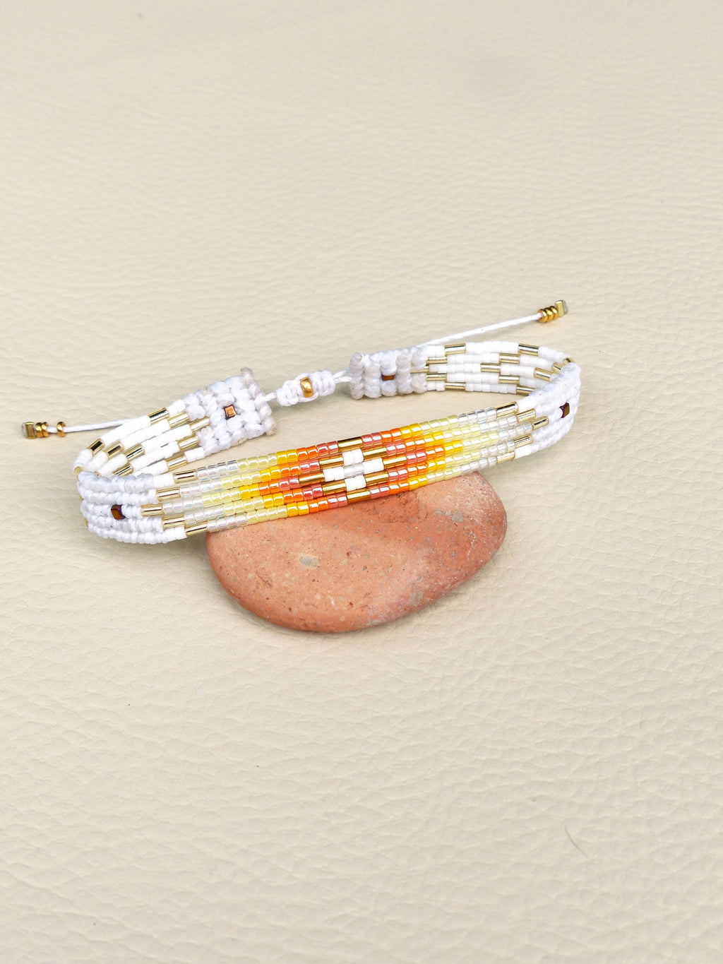Peut inclure: Bracelet en perles blanches avec un motif géométrique coloré dans les tons orange, jaune et rouge. Le bracelet est noué et présente des accents dorés.
