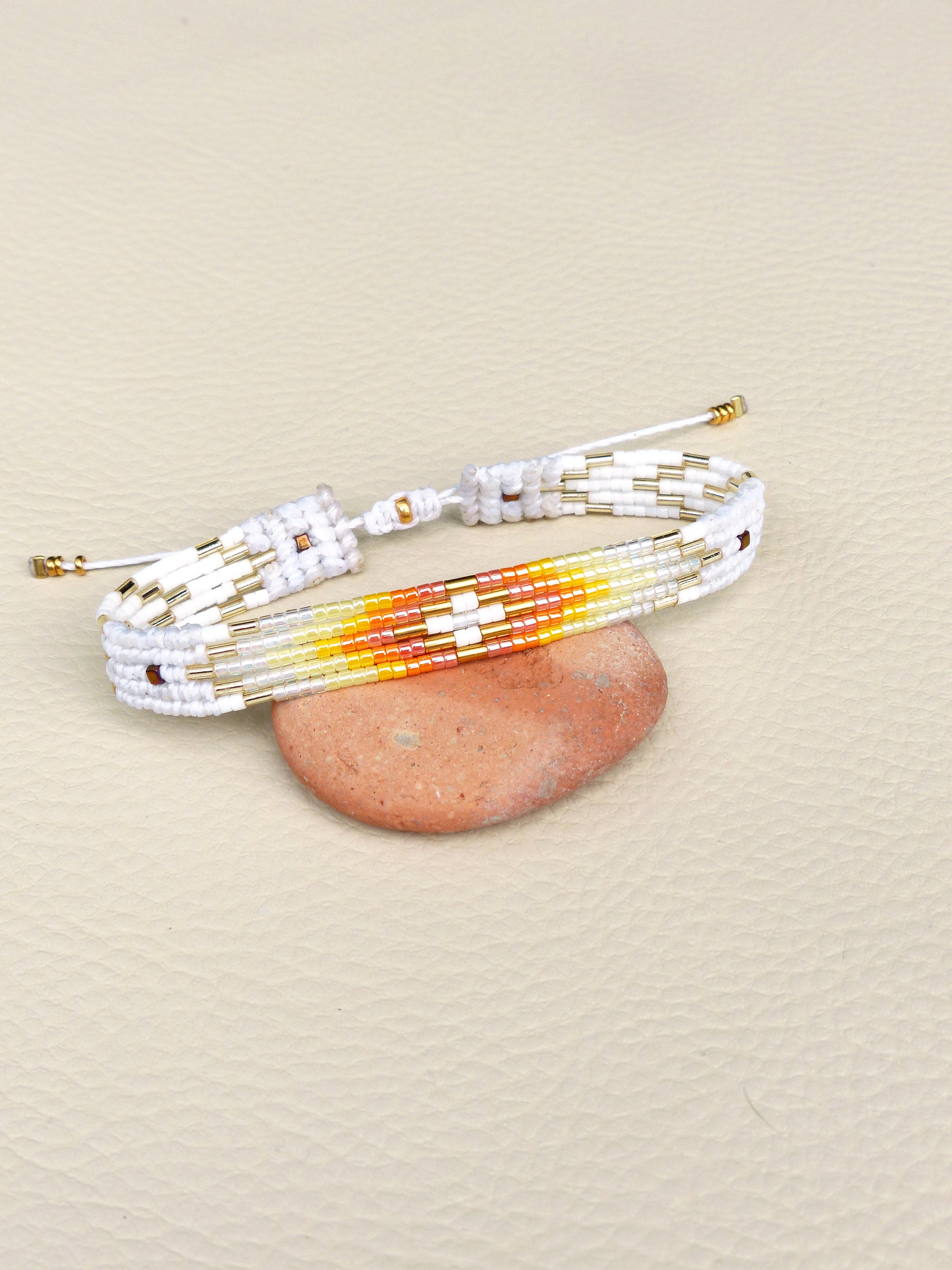 Peut inclure: Bracelet en perles blanches avec un motif géométrique coloré dans les tons orange, jaune et rouge. Le bracelet est noué et présente des accents dorés.