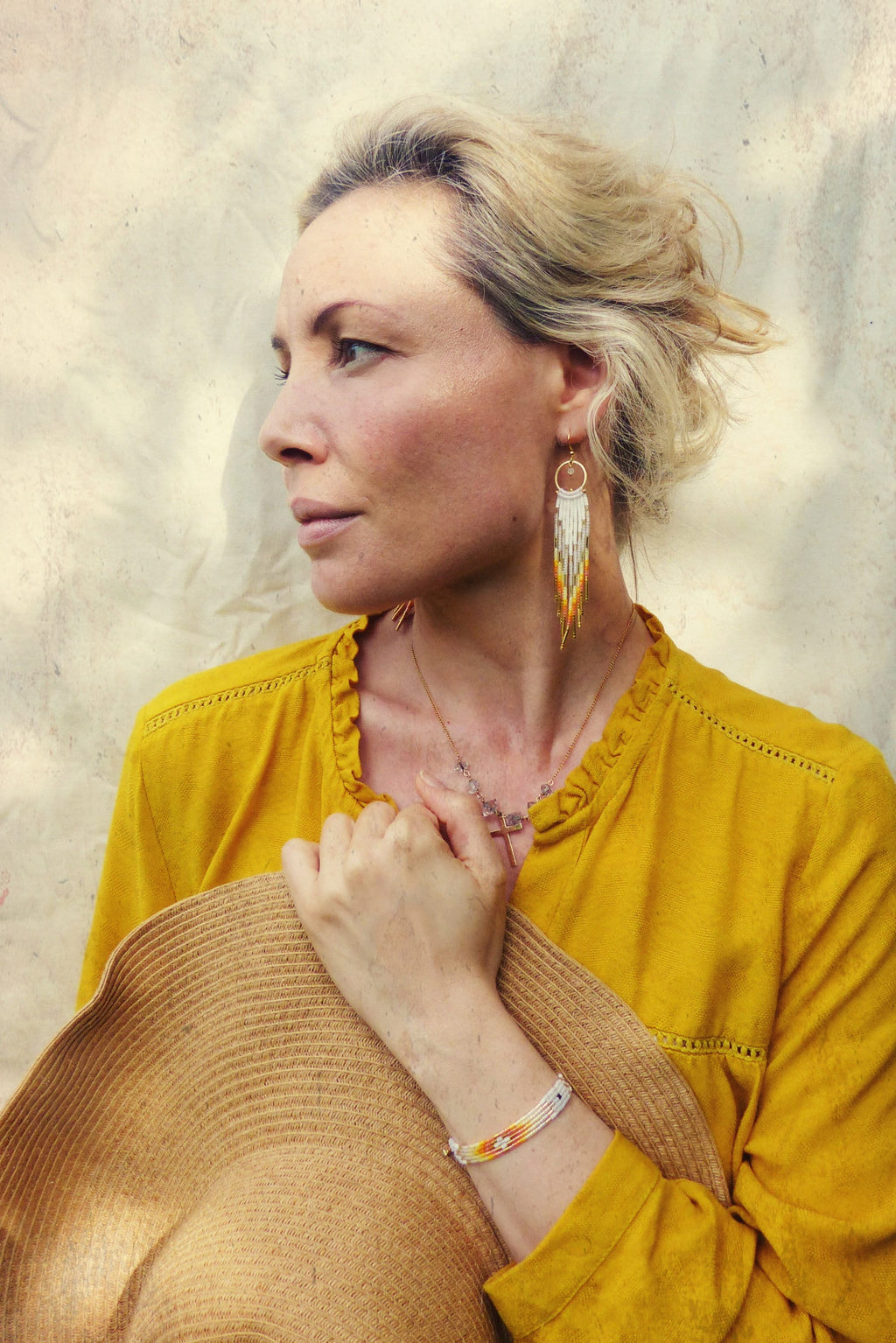 Peut inclure: Une femme portant une chemise jaune et un chapeau de paille, avec de longues boucles d'oreilles en perles et un bracelet en perles. Les boucles d'oreilles et le bracelet sont blancs, orange et dorés.
