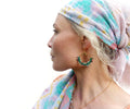 Peut inclure: Une femme portant un foulard à motifs turquoise et rose pâle avec des boucles d'oreilles dorées ornées de perles vertes et multicolores. Les boucles d'oreilles sont en forme de cerceau avec un motif soleil doré.