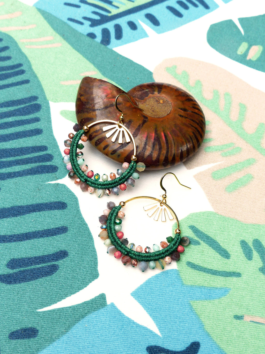 Peut inclure: Une paire de boucles d'oreilles créoles vertes et dorées avec des perles colorées. Les boucles d'oreilles sont faites avec un cordon vert et ont un anneau doré avec un motif en forme d'éventail. Les perles sont un mélange de rouge, rose, vert et marron.