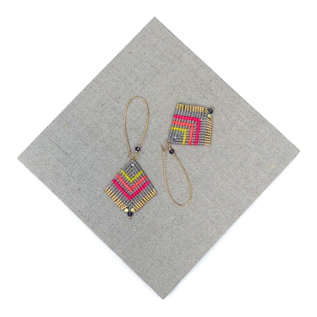 Peut inclure: Une paire de boucles d'oreilles géométriques avec un motif gris, rose et jaune. Les boucles d'oreilles sont faites de petites perles et ont des anneaux dorés.