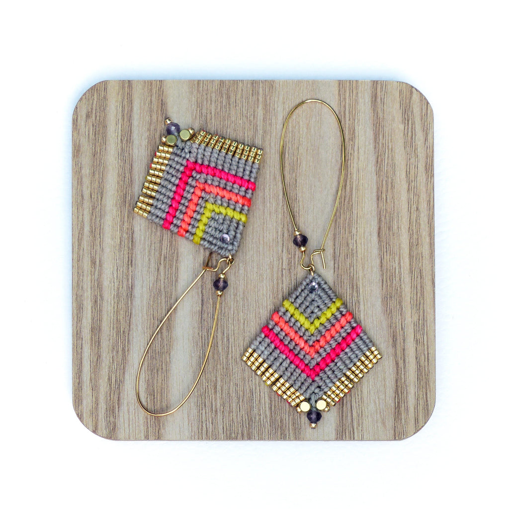 Peut inclure: Une paire de boucles d'oreilles géométriques avec un motif gris, rose et jaune. Les boucles d'oreilles sont faites de petites perles et ont des anneaux dorés.
