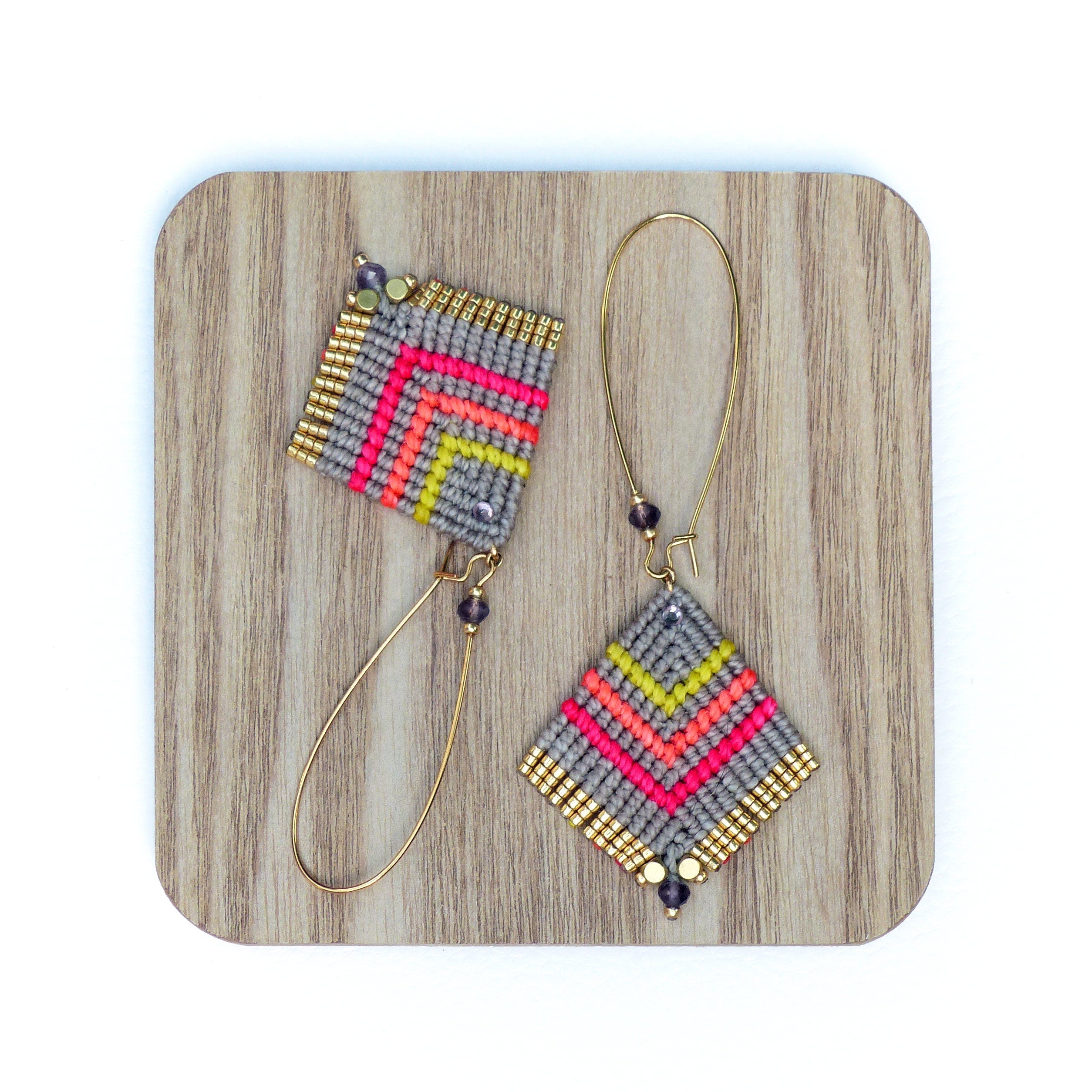 Peut inclure: Une paire de boucles d'oreilles géométriques avec un motif gris, rose et jaune. Les boucles d'oreilles sont faites de petites perles et ont des anneaux dorés.