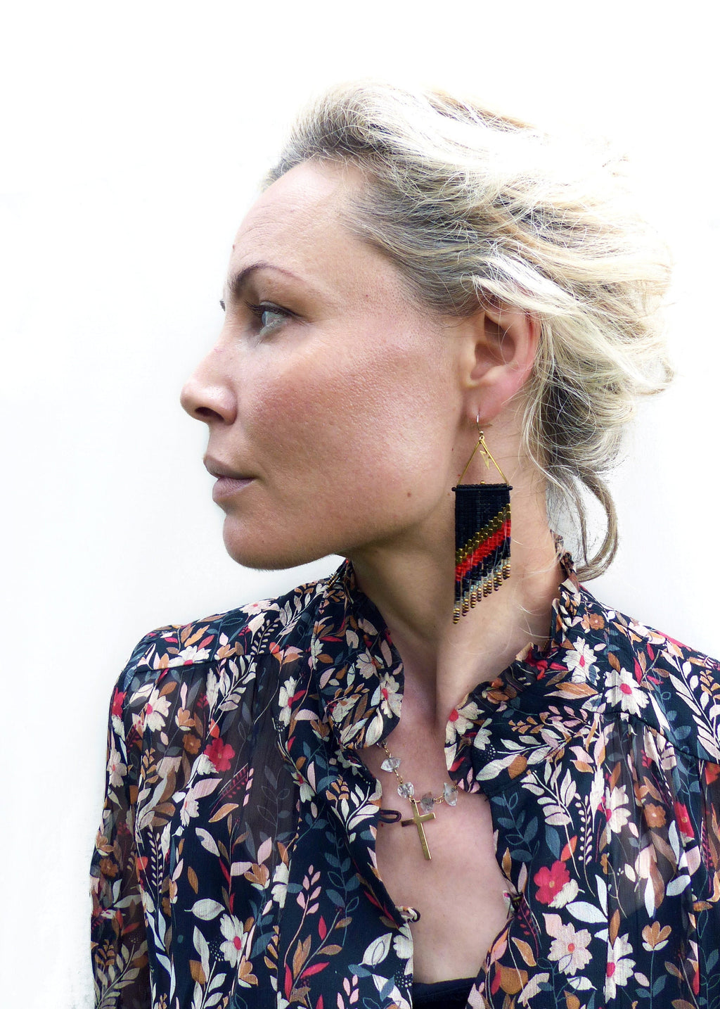 Peut inclure: Une femme porte une boucle d'oreille noire, rouge et dorée. La boucle d'oreille est de forme géométrique avec un crochet doré. Elle porte un chemisier à imprimé floral et un collier.