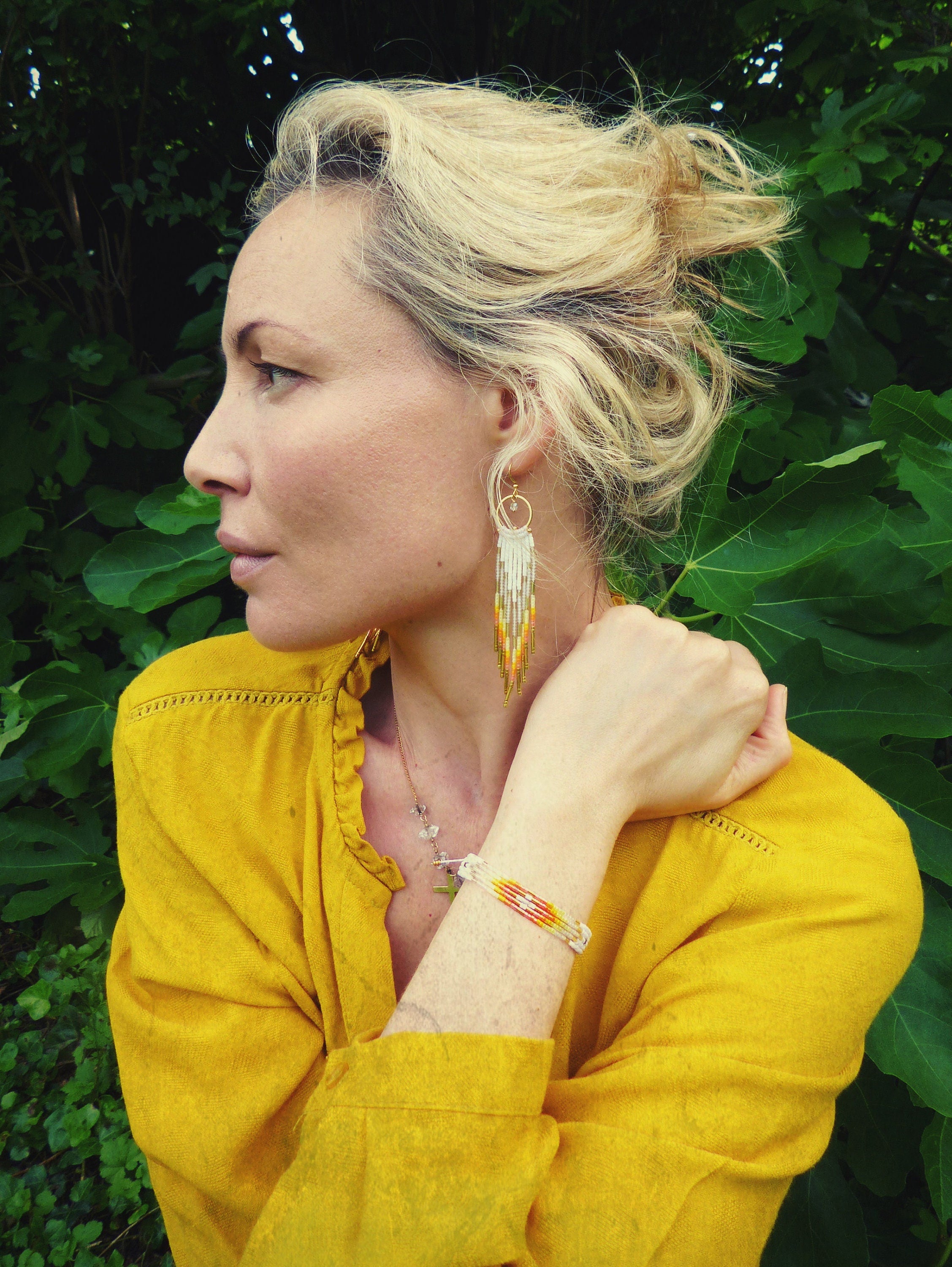 Peut inclure: Une femme portant un chemisier jaune avec un bracelet en perles et de longues boucles d'oreilles en perles. Les boucles d'oreilles sont blanches, dorées et orange.