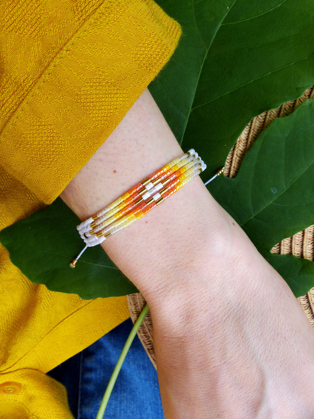 Peut inclure: Un bracelet multi-colore en perles avec des perles orange, jaunes et blanches. Le bracelet est attaché avec une ficelle blanche et a une perle dorée à l'extrémité.