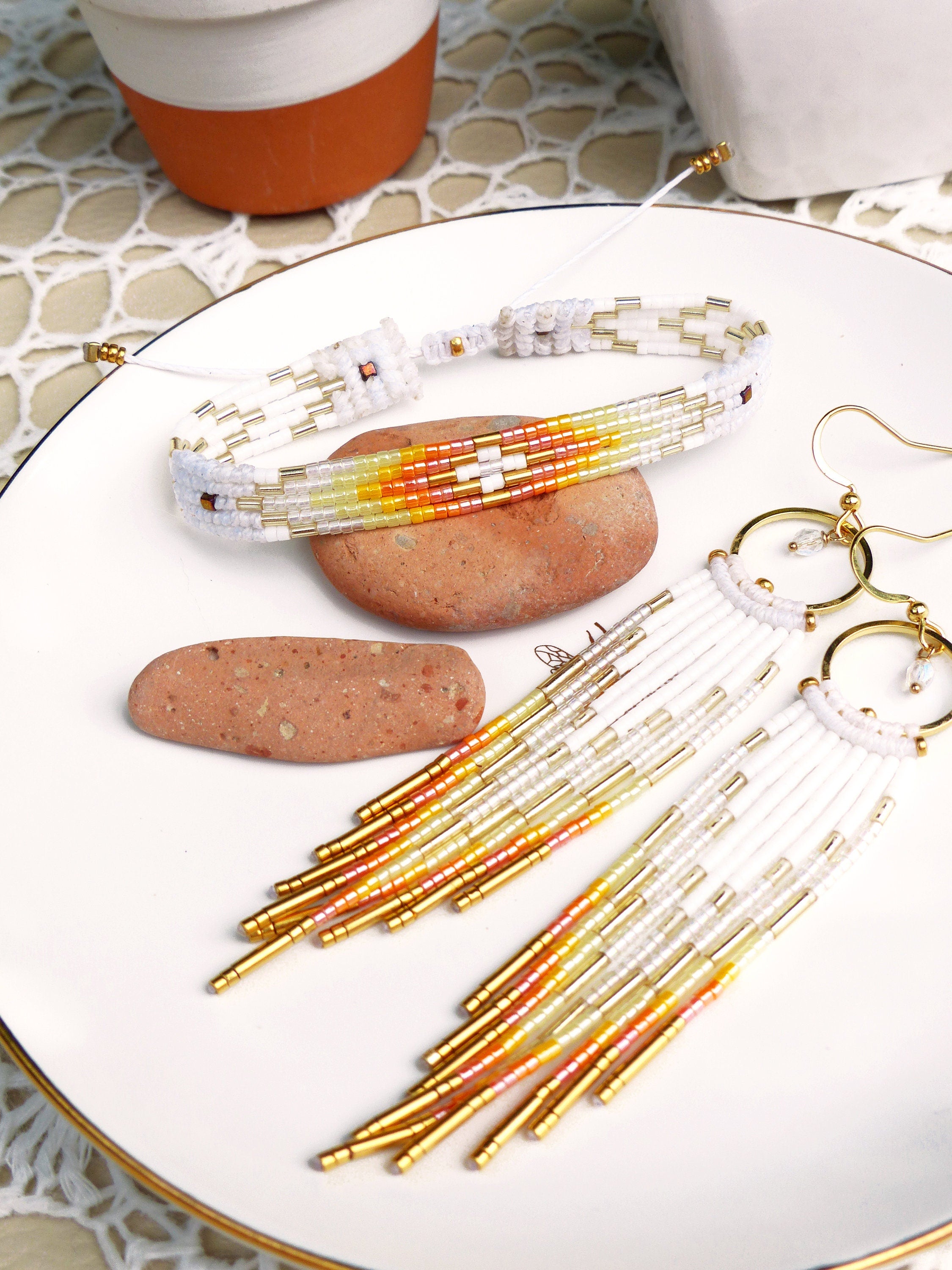 Peut inclure: Un ensemble de bijoux en perles blanches et dorées avec des accents orange et jaunes. L'ensemble comprend un bracelet et une paire de longues boucles d'oreilles.