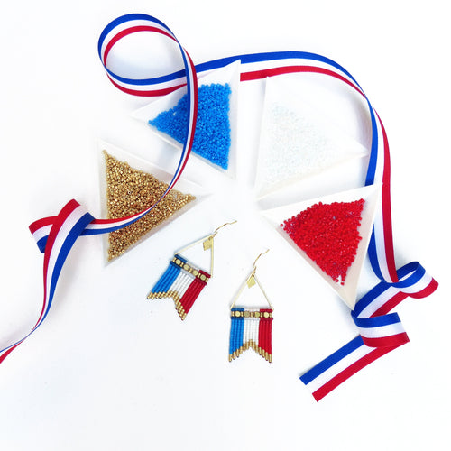 Peut inclure: Boucles d'oreilles faites à la main avec un motif de drapeau, composées de perles bleues, blanches et rouges. Les boucles d'oreilles sont présentées avec de petits contenants triangulaires de perles bleues, blanches, rouges et dorées, et un ruban tricolore.