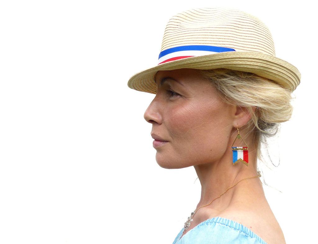 Peut inclure: Une femme porte un chapeau de paille orné d'une bande rayée rouge, blanche et bleue. Elle porte également des boucles d'oreilles triangulaires dorées avec un motif de drapeau rouge, blanc et bleu. Le thème est patriotique.
