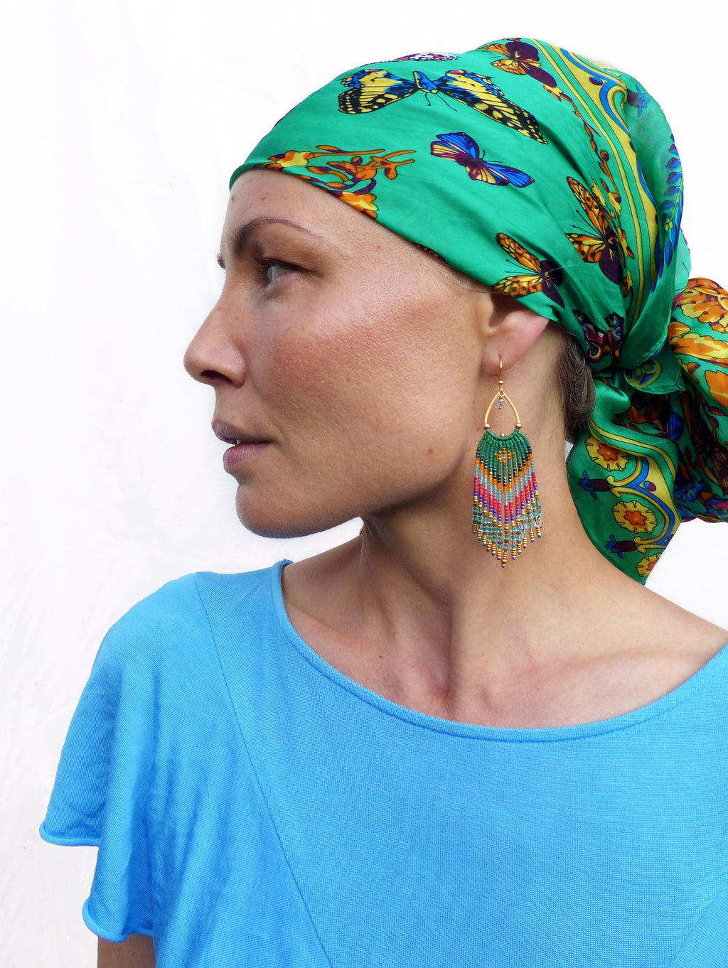 Peut inclure: Une femme portant un foulard vert à imprimé papillon et une paire de longues boucles d'oreilles en perles. Les boucles d'oreilles sont vertes, bleues et roses.