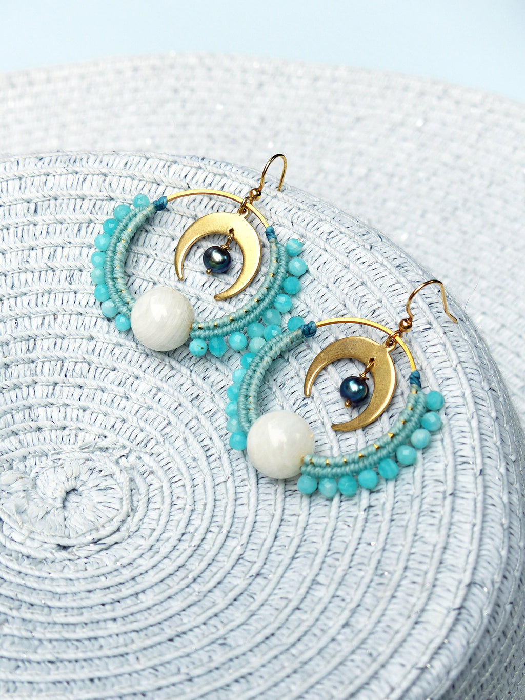 Peut inclure: Une paire de boucles d'oreilles créoles dorées avec un charme de croissant de lune et des perles blanches et bleues.