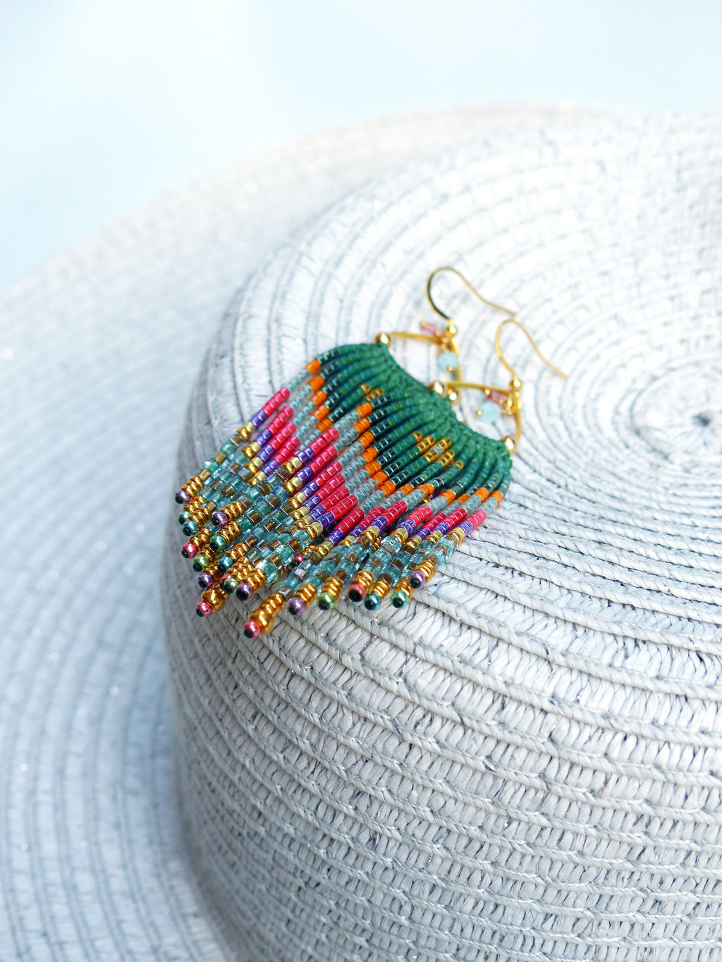 Peut inclure: Une paire de longues boucles d'oreilles en perles colorées avec des anneaux dorés. Les boucles d'oreilles présentent un mélange de perles vertes, bleues, roses, orange et dorées.