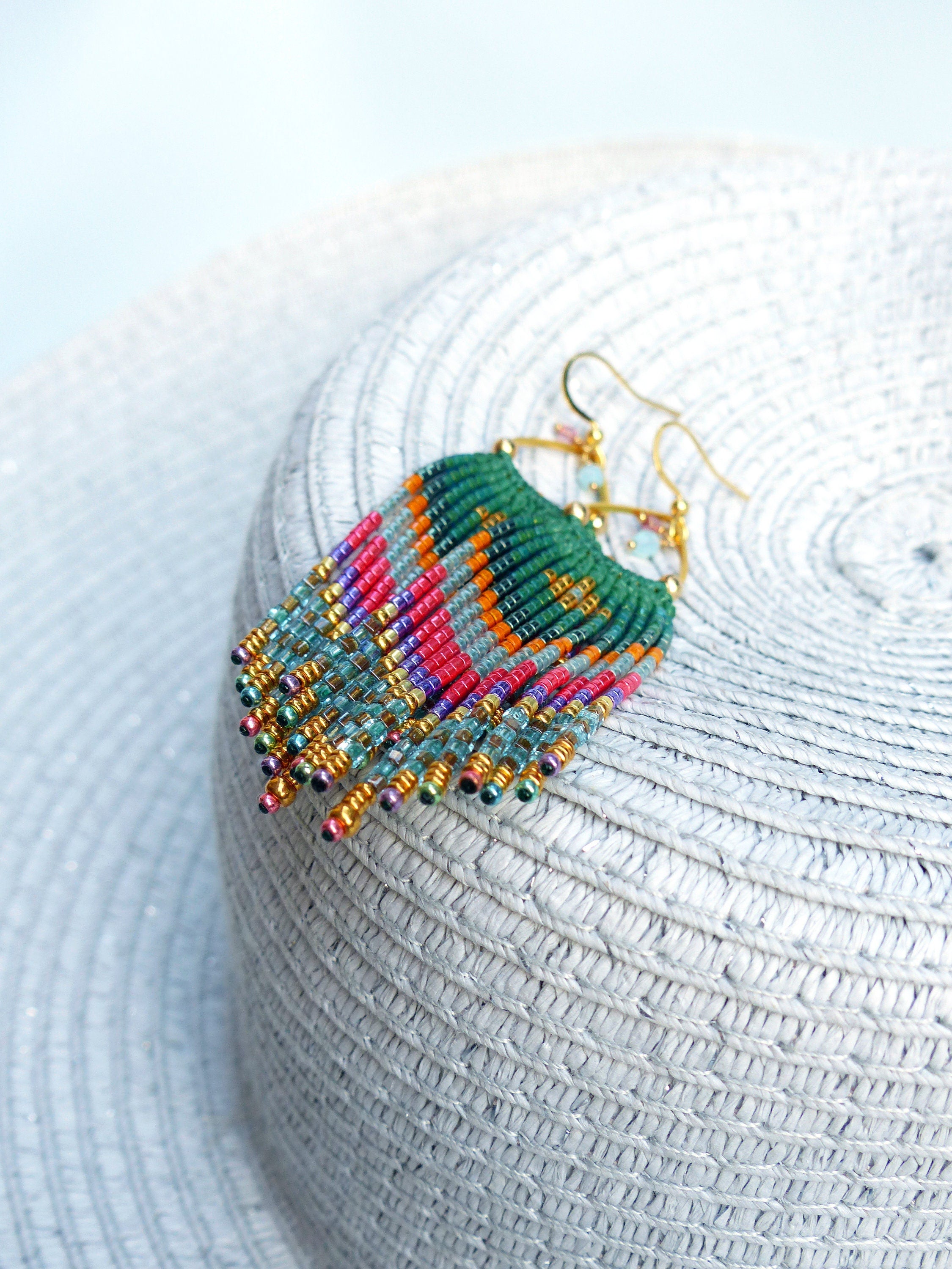 Peut inclure: Une paire de longues boucles d'oreilles en perles colorées avec des anneaux dorés. Les boucles d'oreilles présentent un mélange de perles vertes, bleues, roses, orange et dorées.