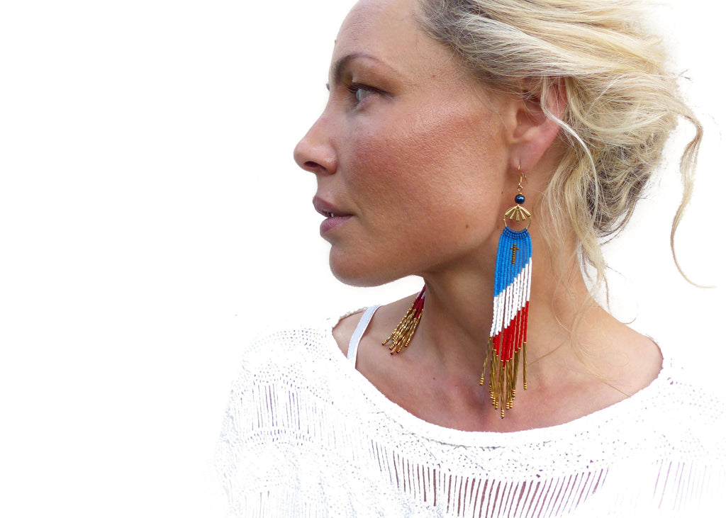 Peut inclure: Une paire de longues boucles d'oreilles en perles avec un motif bleu, blanc et rouge. Les boucles d'oreilles ont un dessus en métal doré avec une petite perle bleue. 