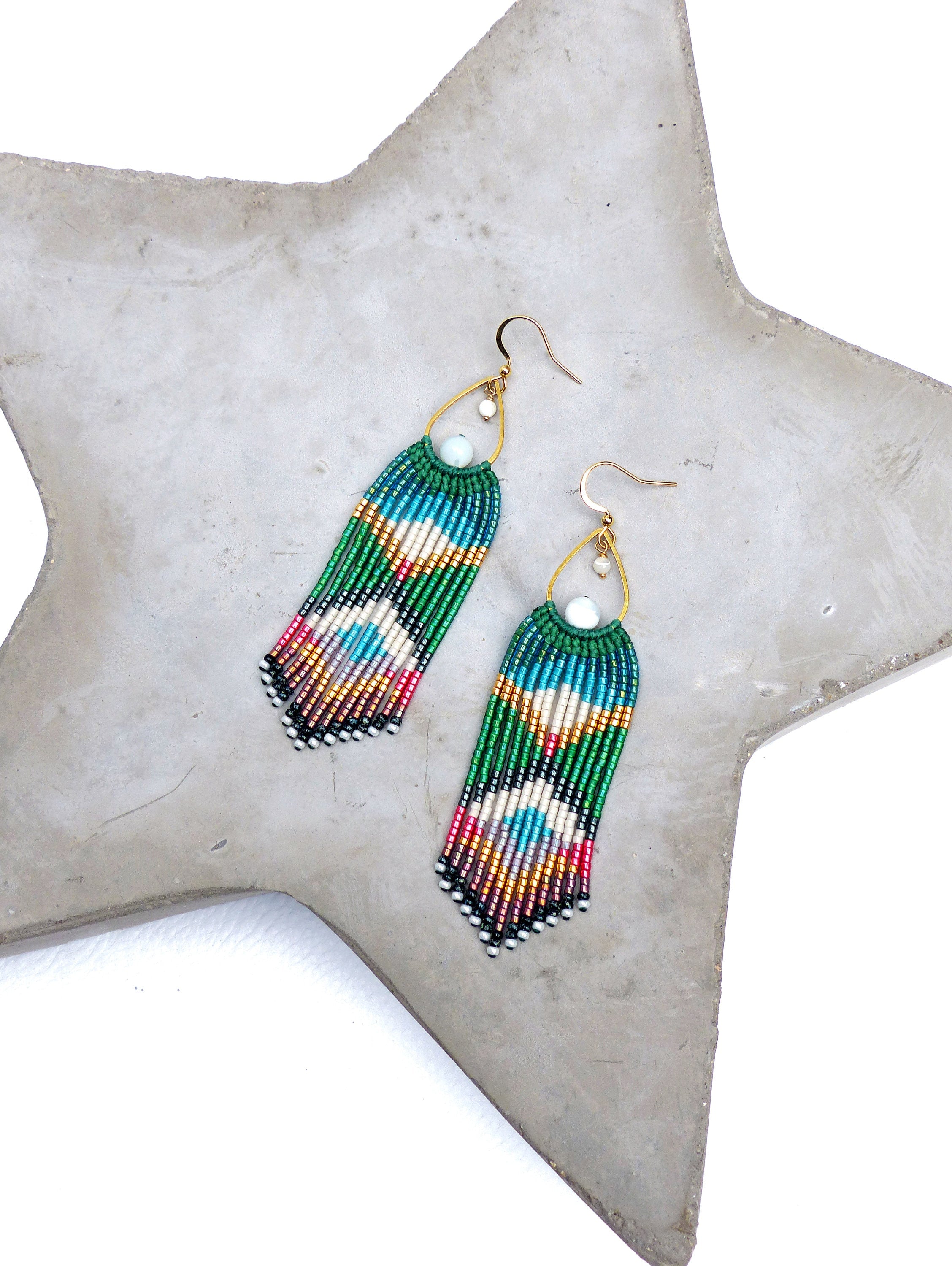 Peut inclure: Une paire de longues boucles d'oreilles pendantes en perles avec un motif de couleurs vert, bleu, blanc, rose et or. Les boucles d'oreilles présentent une perle de pierre blanche en haut et un crochet en or.