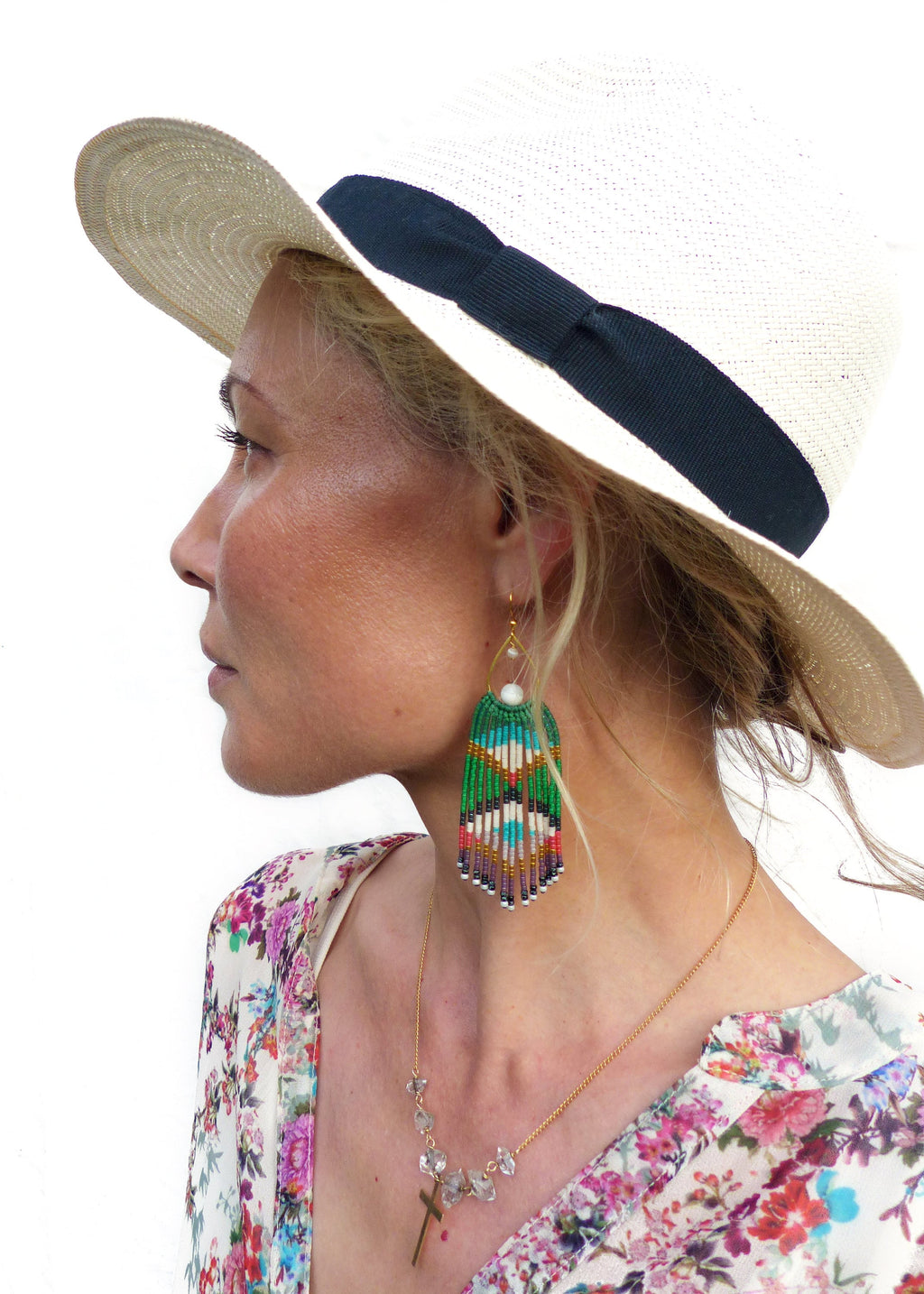Peut inclure: Une femme portant un chapeau de paille blanc avec un ruban noir, une blouse à imprimé floral et de longues boucles d'oreilles en perles avec un motif vert, blanc et bleu. Elle porte également un collier en chaîne dorée avec un pendentif en cristal.