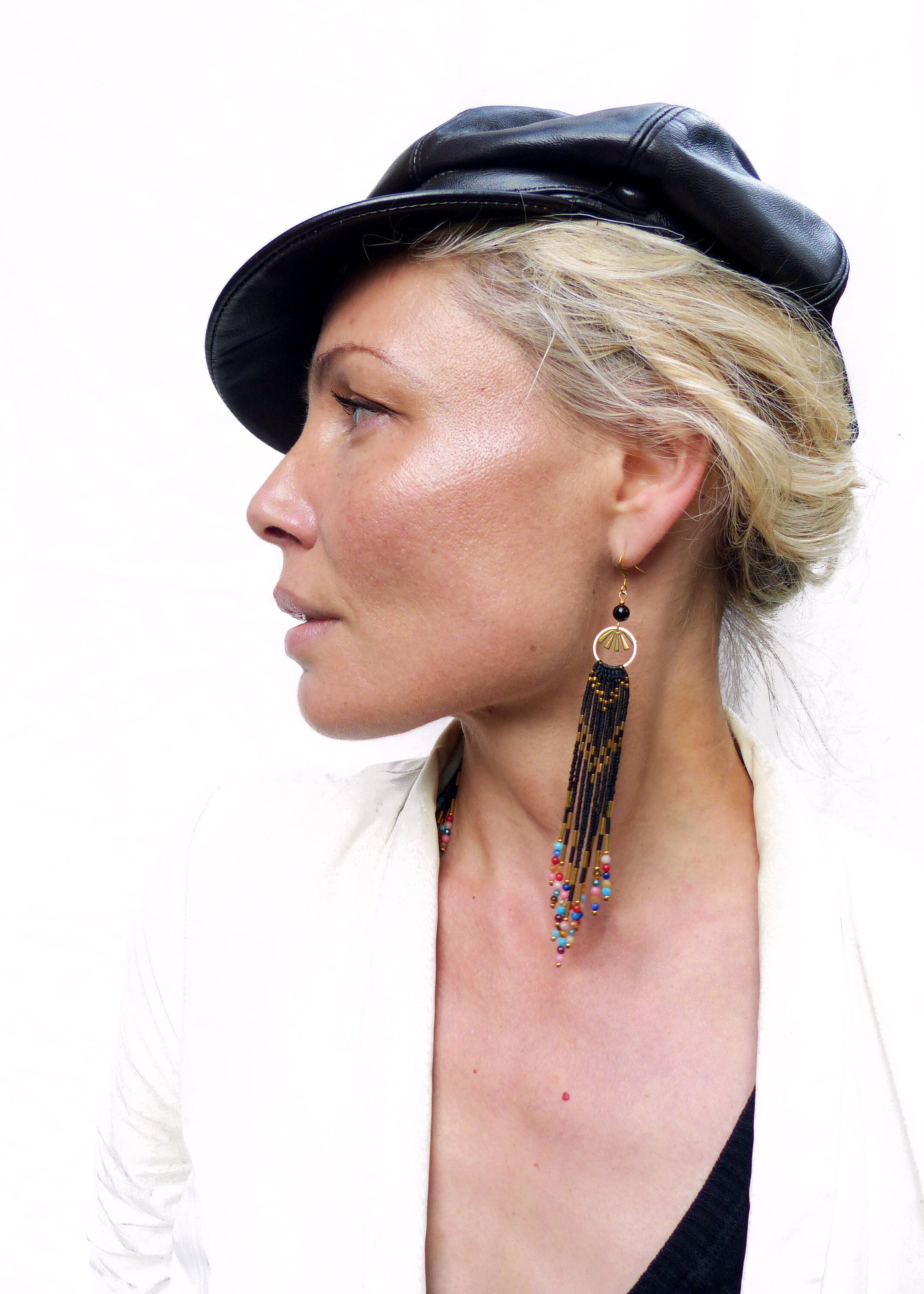 Peut inclure: Une femme portant une casquette en cuir noir et un blazer blanc avec de longues boucles d'oreilles en perles noires avec des accents colorés.