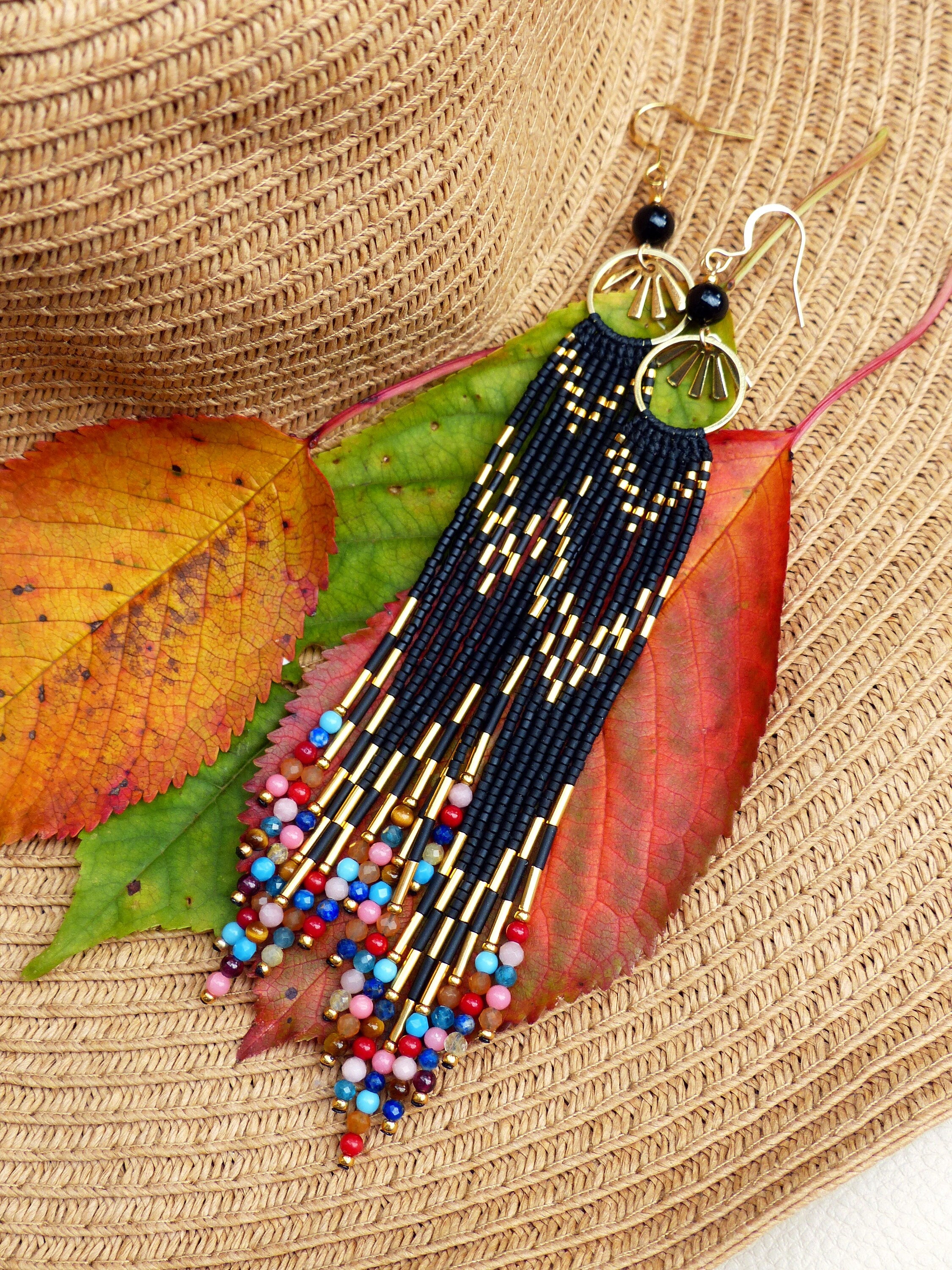 Peut inclure: Longues boucles d'oreilles en perles noires et dorées avec des accents de pierres précieuses colorées. Les boucles d'oreilles sont suspendues à un chapeau de paille avec des feuilles d'automne.