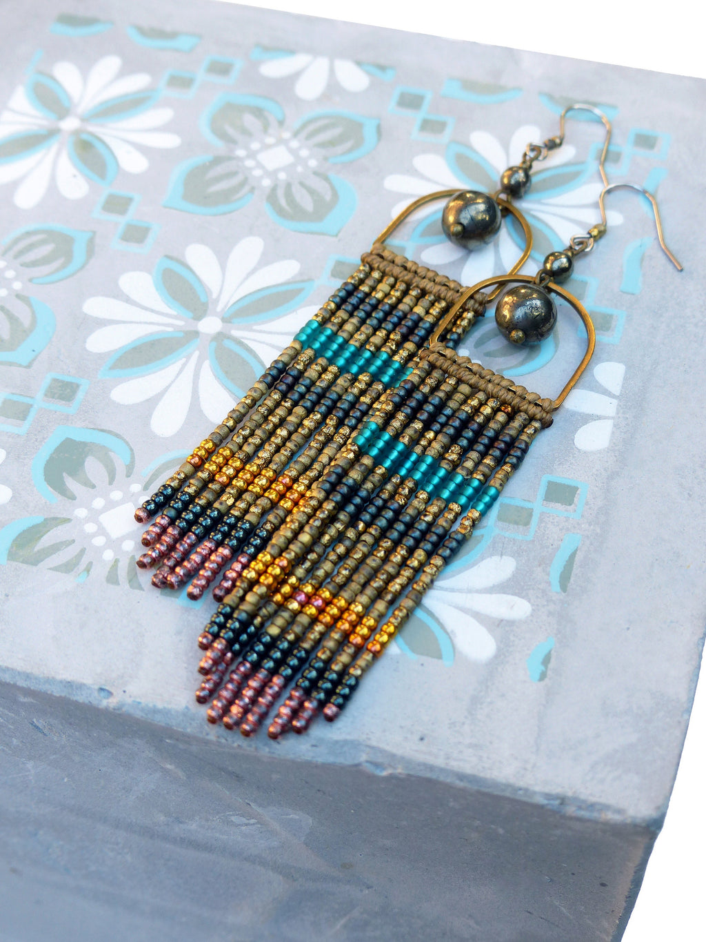 Peut inclure: Une paire de longues boucles d'oreilles en perles avec un motif géométrique. Les boucles d'oreilles sont faites de perles dorées, noires, turquoise et cuivrées. Les boucles d'oreilles ont un simple anneau en laiton en haut et pendent jusqu'à environ 7,5 cm.