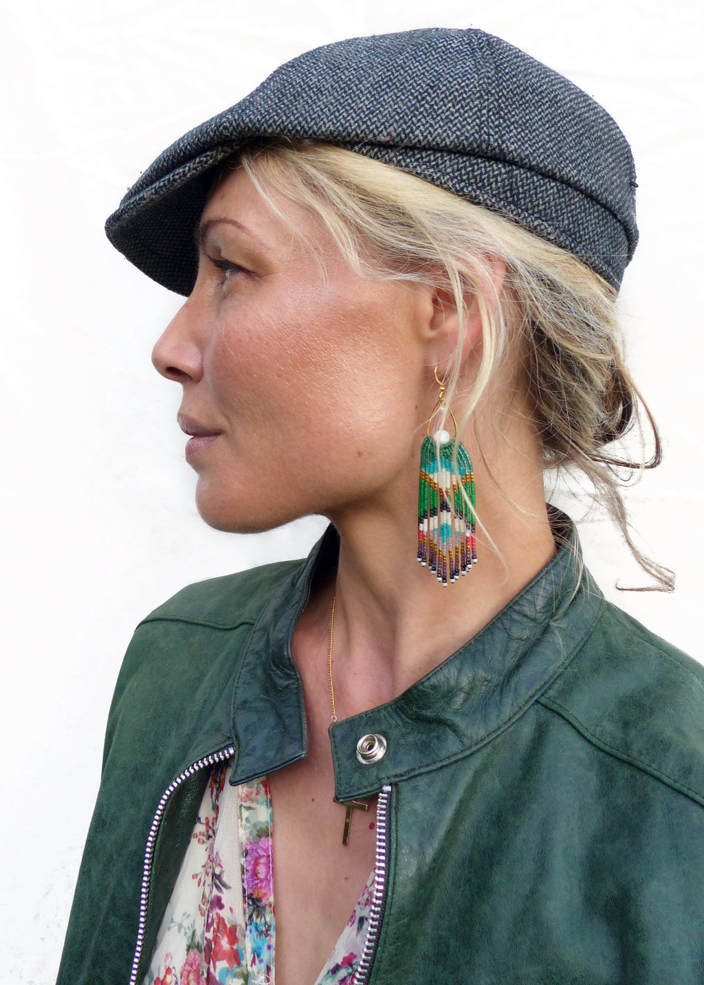 Peut inclure: Une femme portant une veste en cuir verte, un chemisier à imprimé floral, une casquette de newsboy en tweed gris et de longues boucles d'oreilles en perles. 