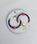 Peut inclure: Une paire de boucles d'oreilles créoles avec un design de perles bordeaux et noires. Les boucles d'oreilles ont un anneau en fil d'or et un petit charme en perle.