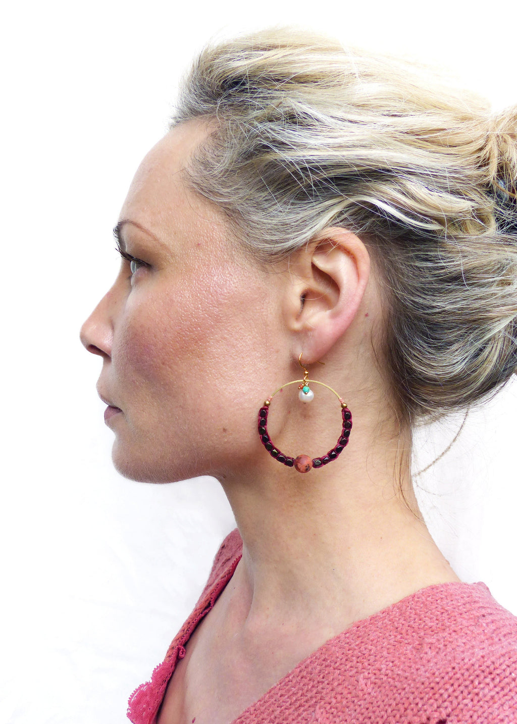 Peut inclure: Une femme portant un pull rouge avec une boucle d'oreille en or en forme de cercle ornée de perles bordeaux et d'un charme en perle blanche.