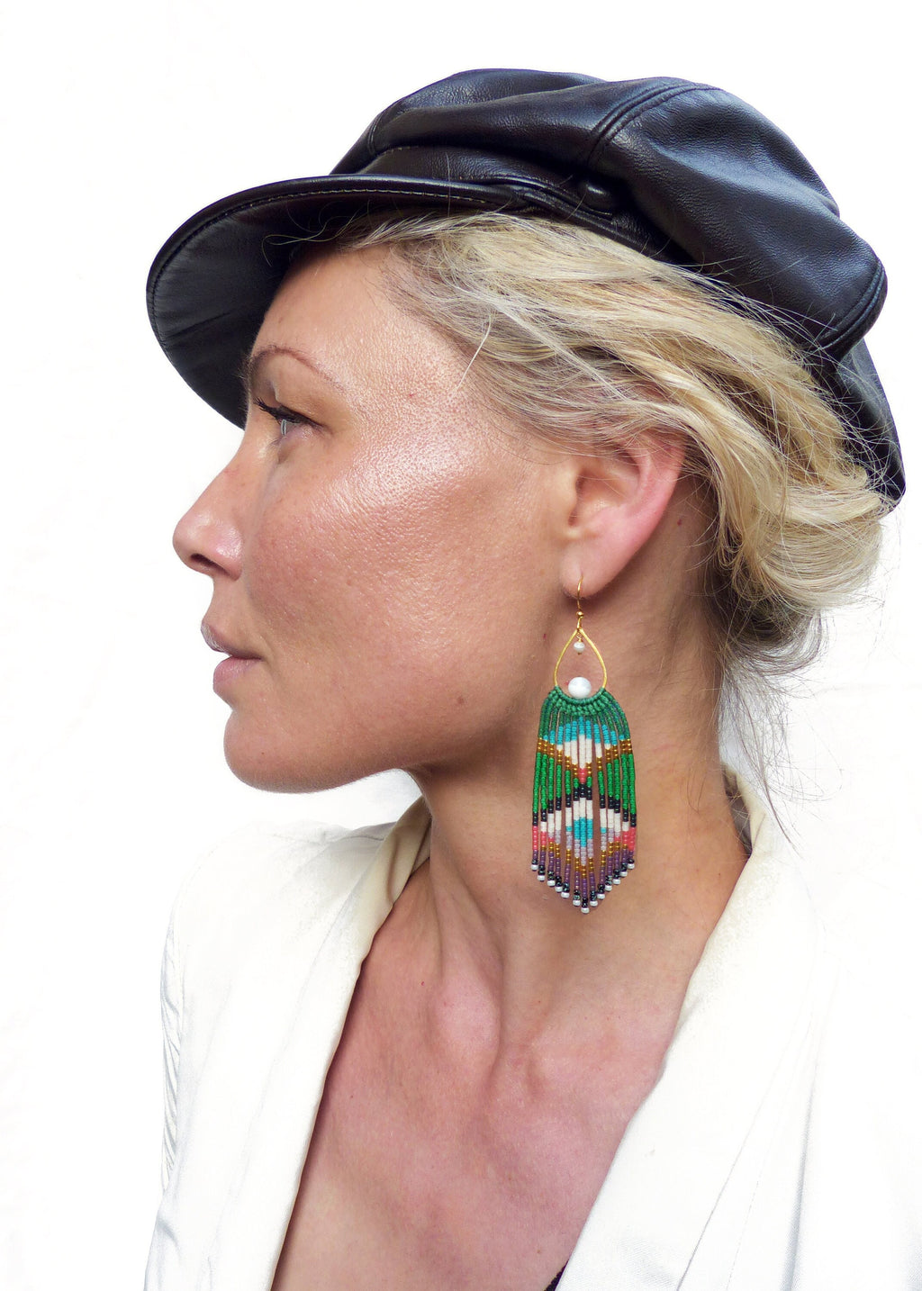 Peut inclure: Une femme portant une casquette en cuir noir et un blazer blanc avec de longues boucles d'oreilles en perles vertes et multicolores.