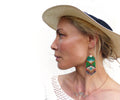 Peut inclure: Une femme portant un chapeau de paille blanc avec un bandeau noir, un haut en crochet blanc et un collier en or avec un pendentif en cristal. Elle porte de longues boucles d'oreilles en perles vertes avec une perle blanche au centre.