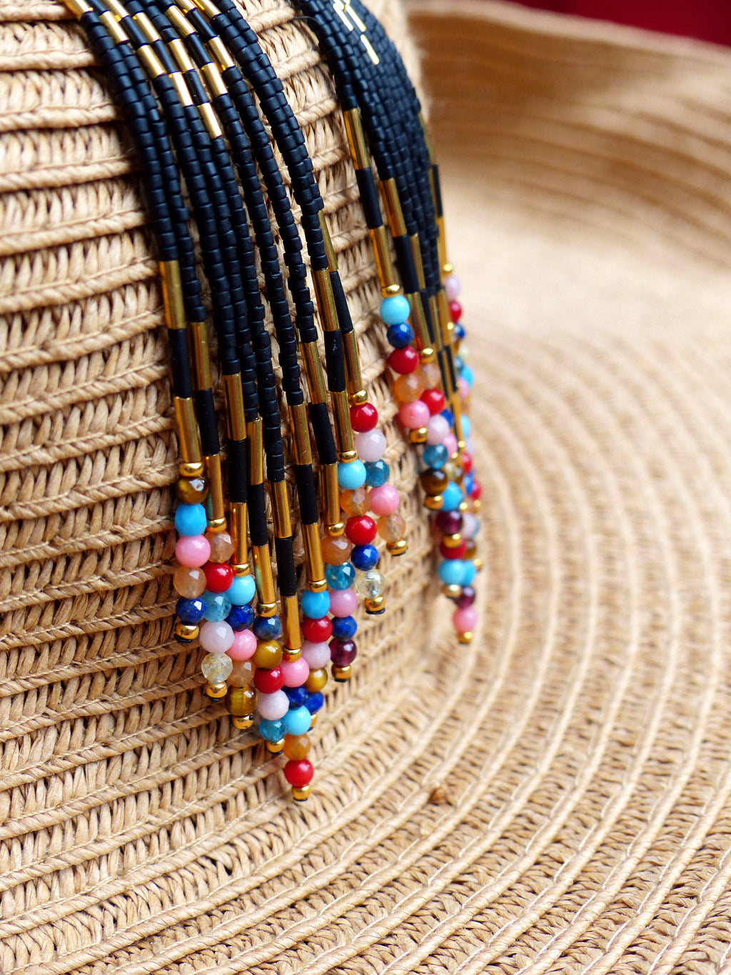 Peut inclure: Gros plan d'un collier de perles coloré avec des accents noirs et dorés. Le collier est suspendu à un chapeau de paille.