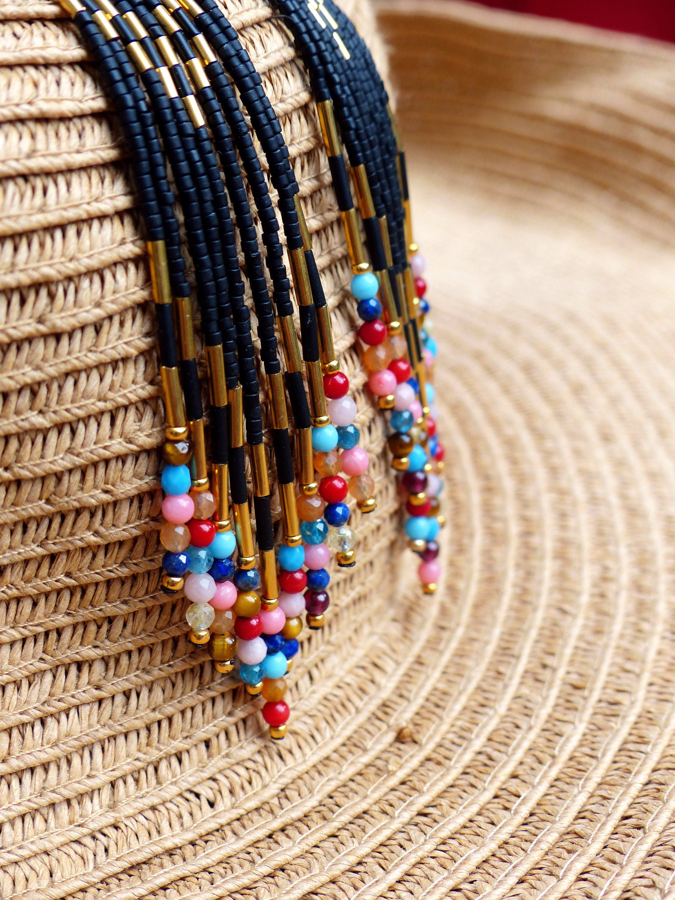 Peut inclure: Gros plan d'un collier de perles coloré avec des accents noirs et dorés. Le collier est suspendu à un chapeau de paille.