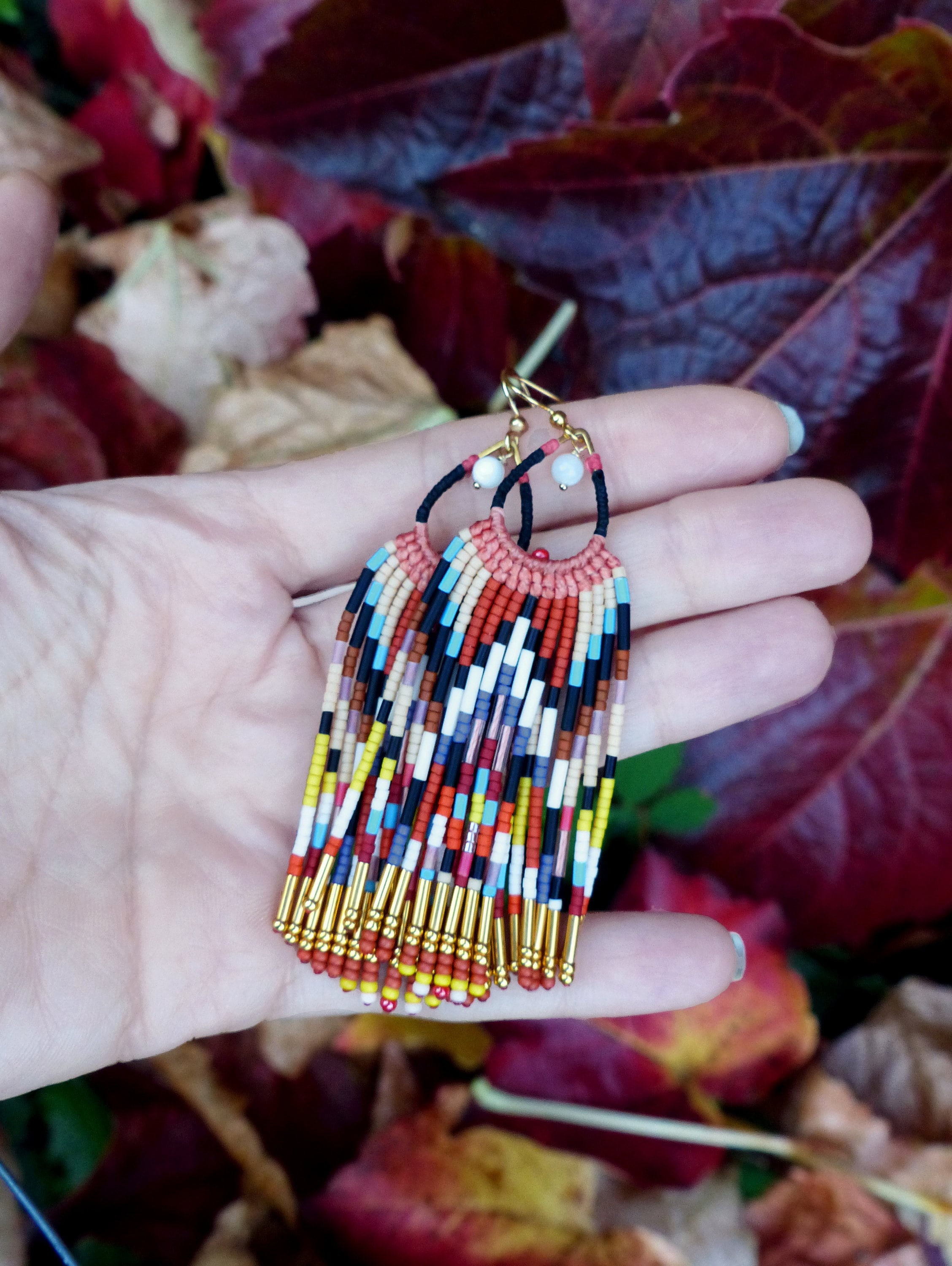 Peut inclure: Une paire de boucles d'oreilles en perles colorées avec des accents dorés. Les boucles d'oreilles sont faites avec une variété de perles dans des tons de rouge, orange, jaune, bleu, vert et noir. Les perles sont enfilées sur un fil doré et les boucles d'oreilles sont terminées par un crochet doré.