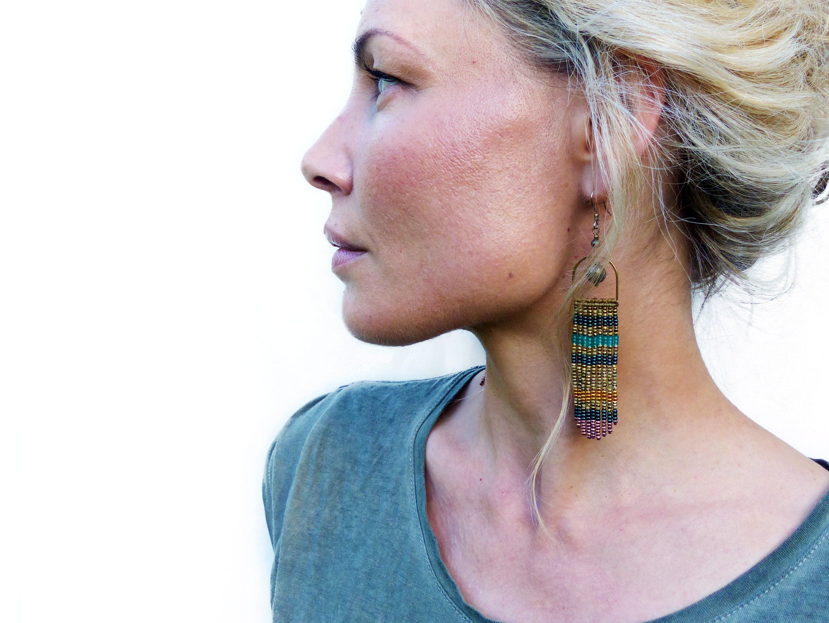 Peut inclure: Une femme portant une chemise verte avec de longues boucles d'oreilles en perles. Les boucles d'oreilles sont faites de perles dorées, brunes, turquoise et violettes.