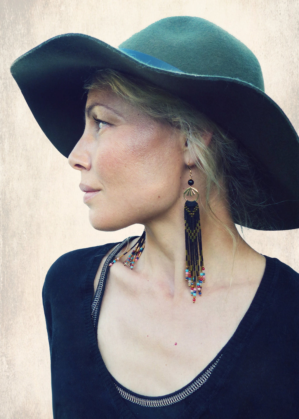Peut inclure: Une femme portant un chapeau fedora en feutre vert et un pull noir avec un collier de perles et de longues boucles d'oreilles en perles. Les boucles d'oreilles sont noires et dorées avec des perles colorées.