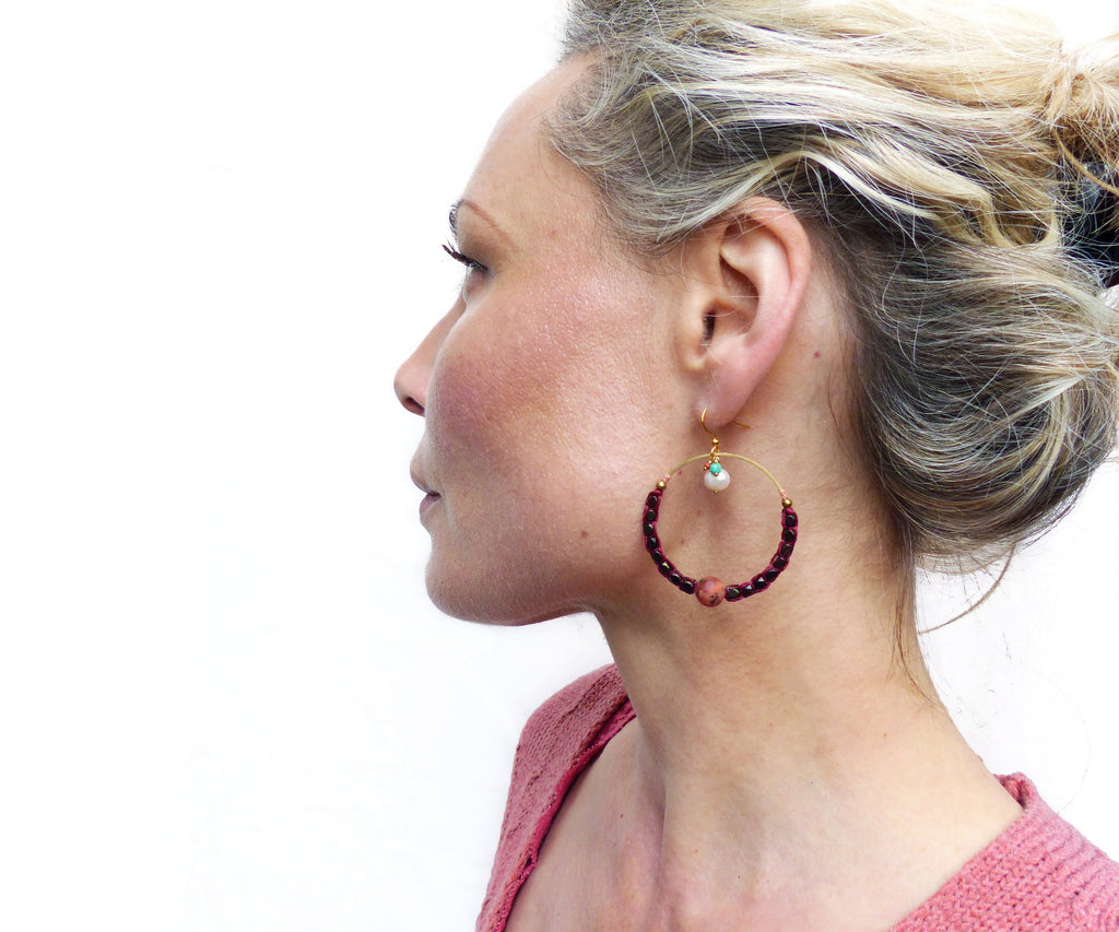 Peut inclure: Boucles d'oreilles créoles dorées avec un design de perles bordeaux et blanches. Les boucles d'oreilles présentent une petite perle blanche et une perle bordeaux plus grande.