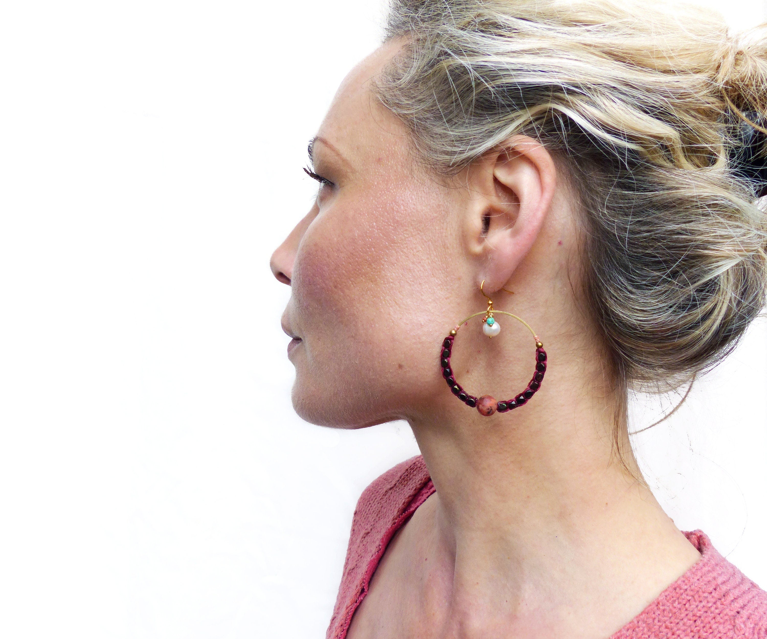 Peut inclure: Boucles d'oreilles créoles dorées avec un design de perles bordeaux et blanches. Les boucles d'oreilles présentent une petite perle blanche et une perle bordeaux plus grande.