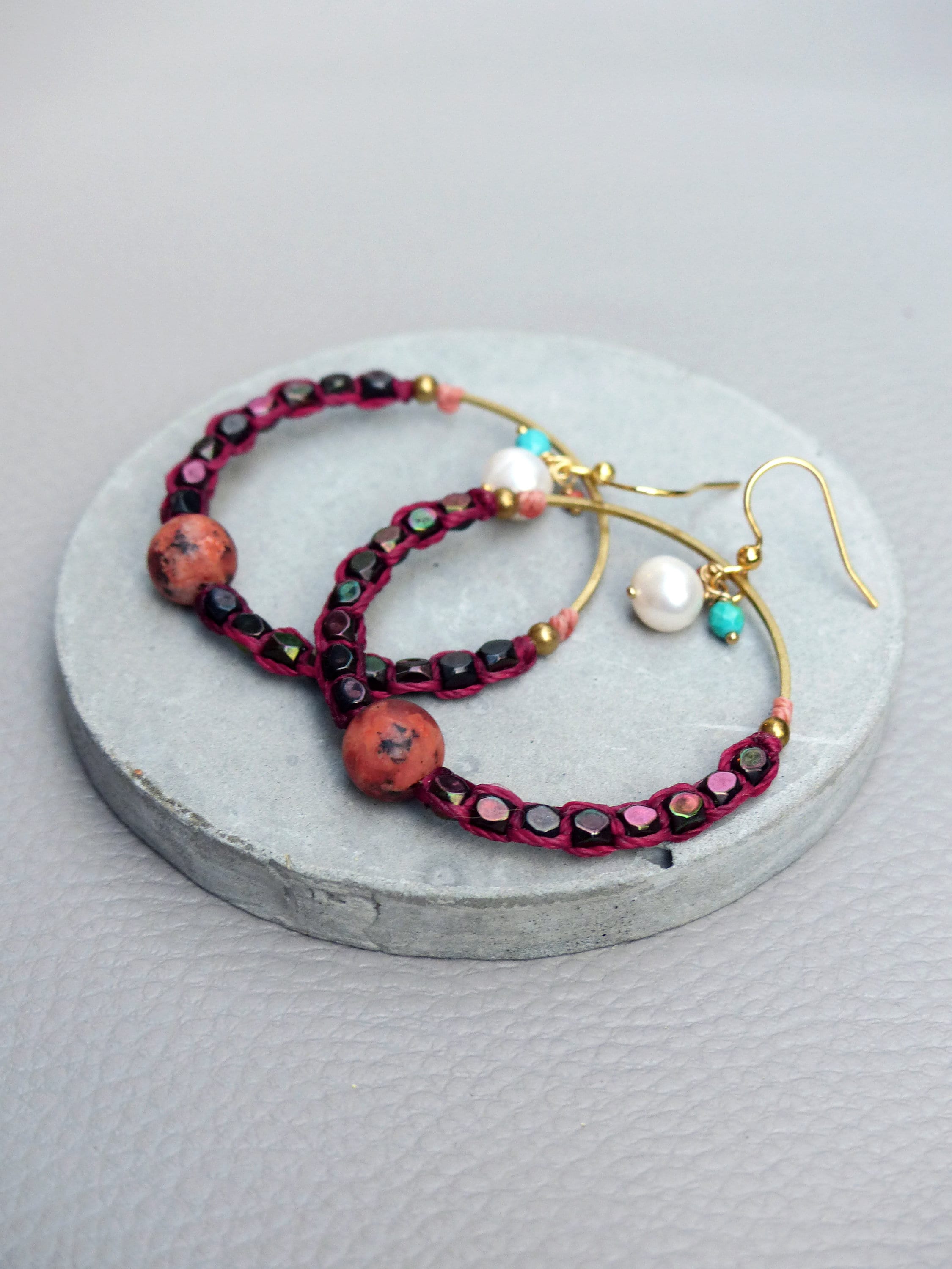 Peut inclure: Une paire de boucles d'oreilles créoles avec un design de perles bordeaux et noires. Les boucles d'oreilles ont un anneau en fil d'or et présentent deux petites perles rondes rouges.