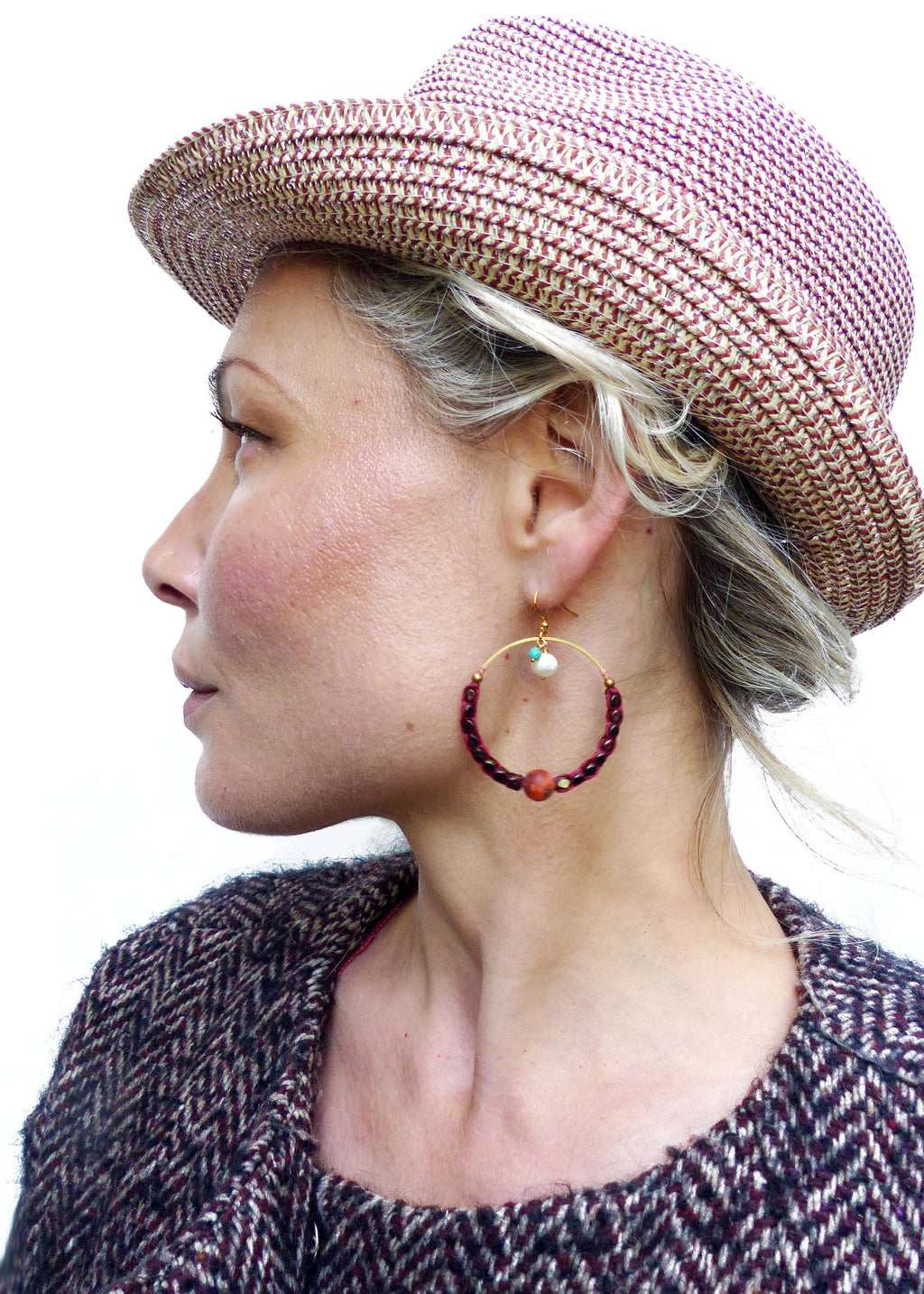 Peut inclure: Une femme portant un chapeau de paille rose et blanc et une veste en tweed marron et blanc. Elle porte de grandes boucles d'oreilles créoles avec des perles rouges, une perle blanche et une perle turquoise.