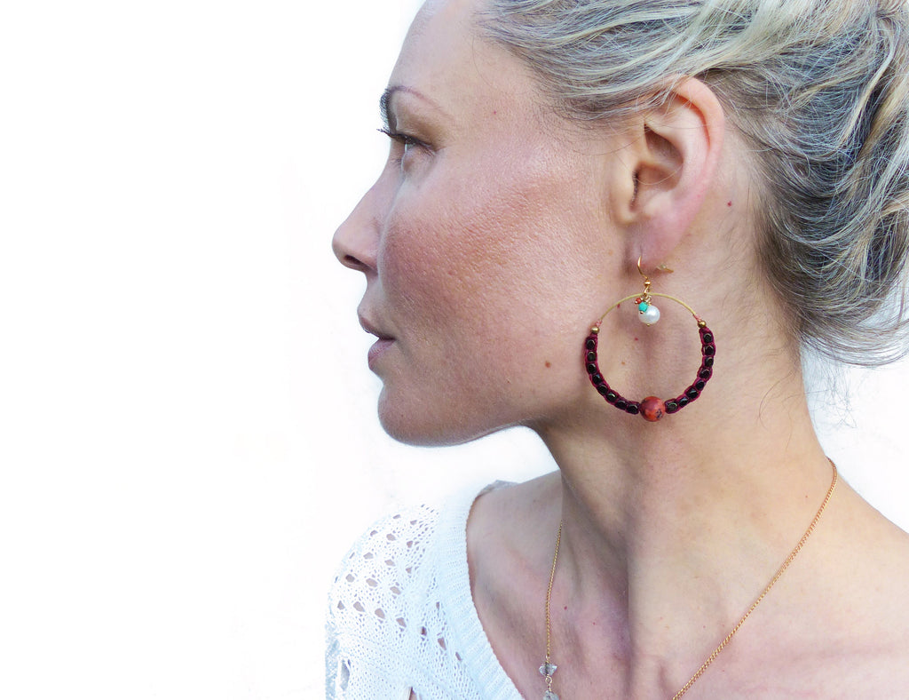 Peut inclure: Une femme portant un haut en crochet blanc et un collier en or avec un petit pendentif. Elle porte une paire de boucles d'oreilles créoles en perles rouge foncé et fil d'or. Les boucles d'oreilles ont une petite perle blanche et une perle turquoise qui pendent.