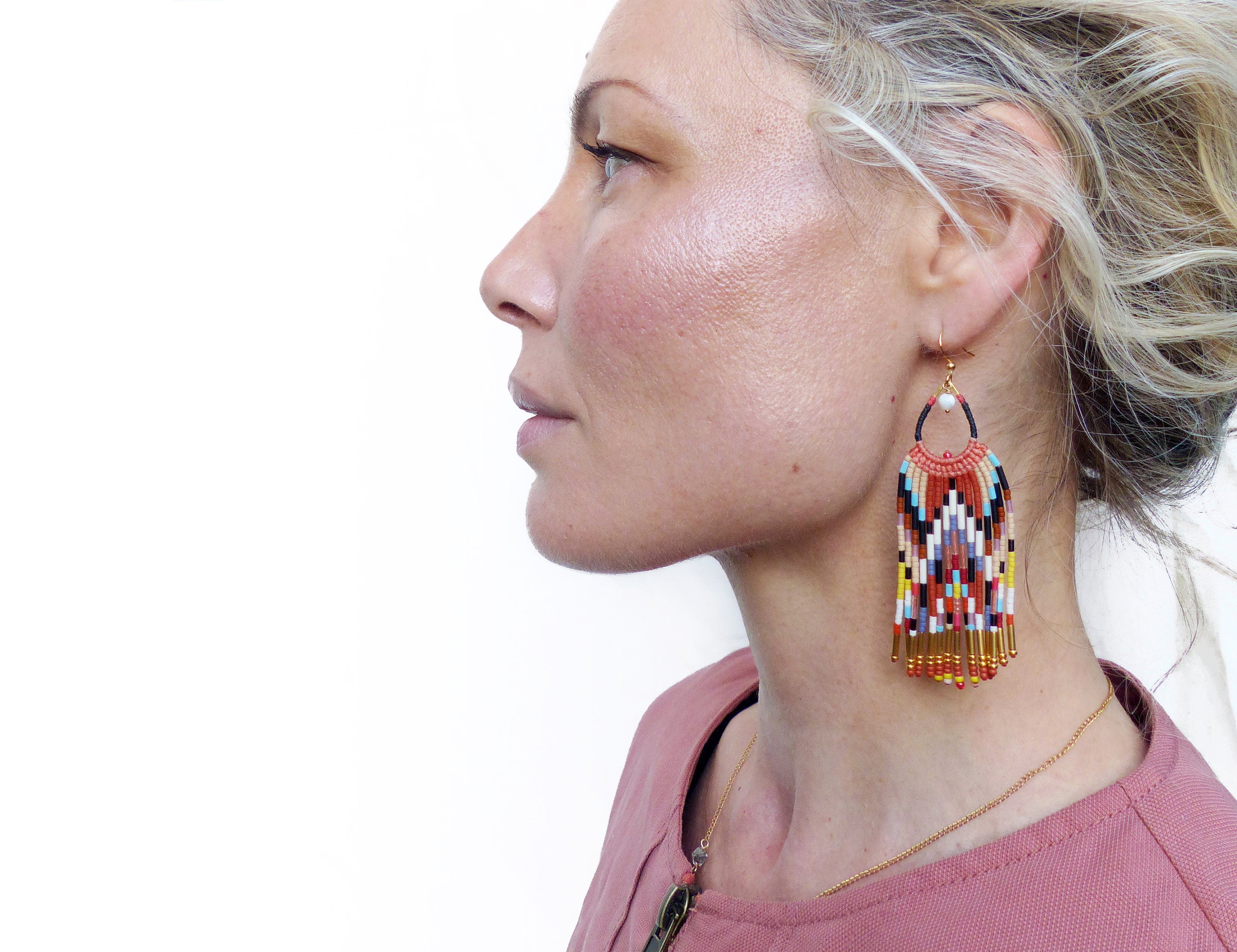 Peut inclure: Une paire de longues boucles d'oreilles en perles colorées avec un motif géométrique et des accents dorés. Les boucles d'oreilles pendent du lobe de l'oreille et ont une frange de perles en bas.