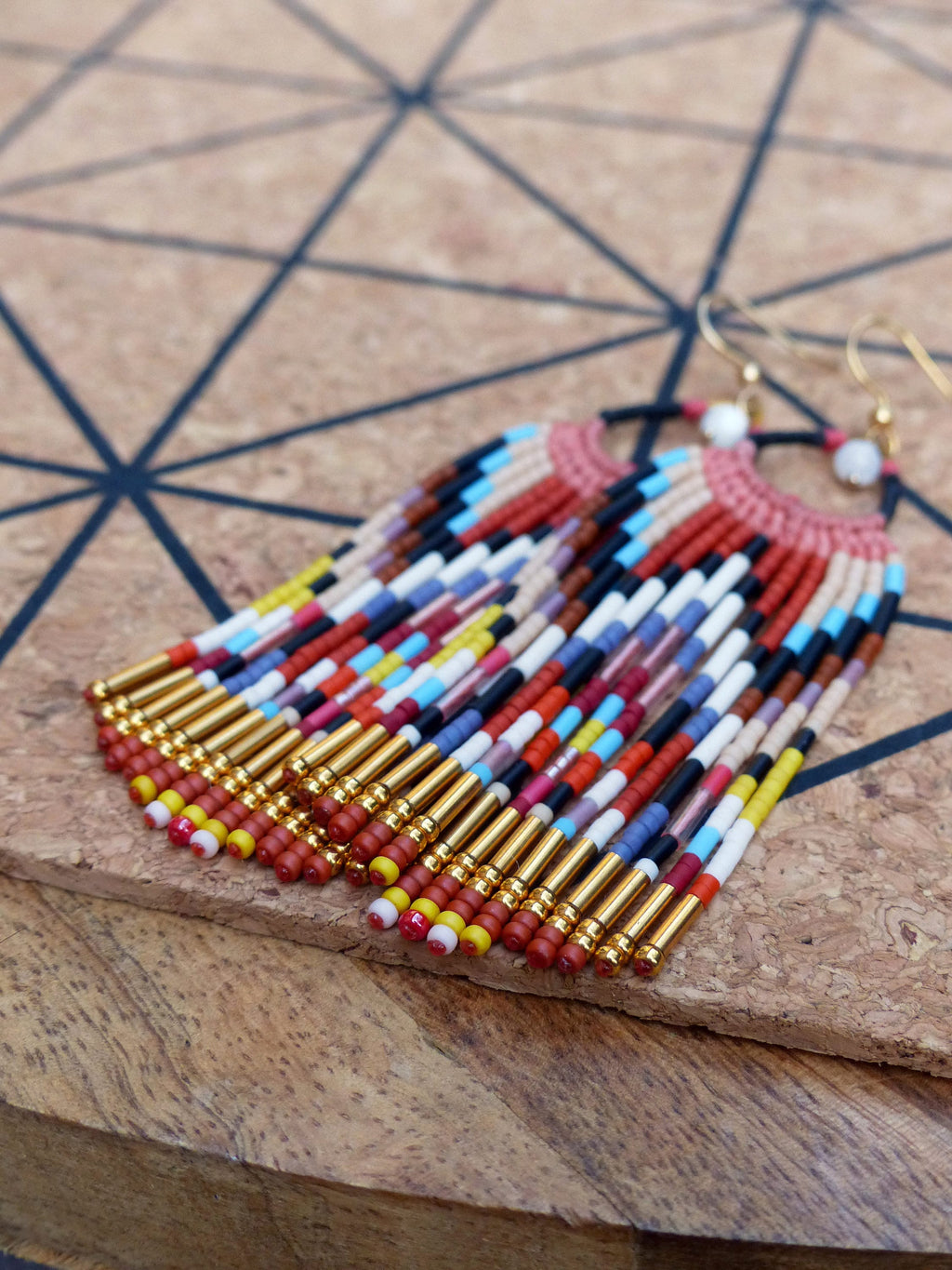 Peut inclure: Une paire de longues boucles d'oreilles en perles colorées avec des accents dorés. Les boucles d'oreilles sont faites avec une variété de perles dans des tons de rouge, bleu, jaune, blanc et noir. Les perles sont enfilées sur un fil doré et les boucles d'oreilles sont terminées par des crochets dorés.